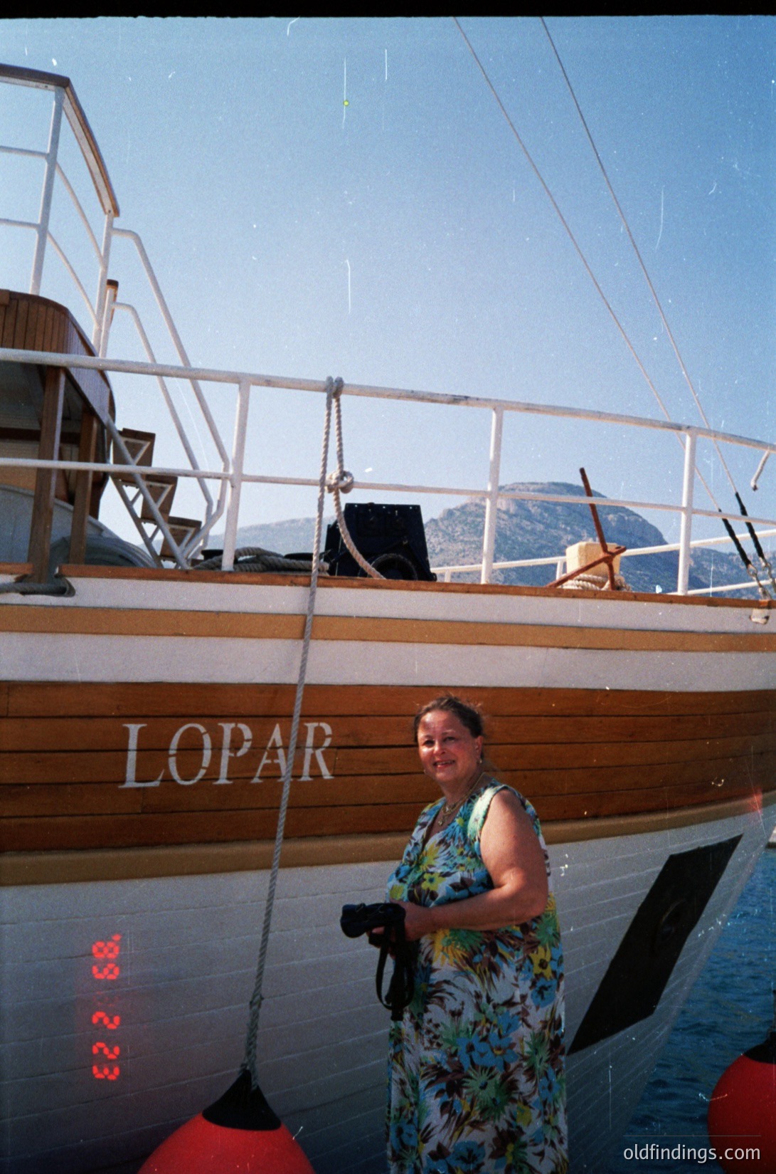 Vintage wooden sailboat named "LOPAR" with a woman in floral dress posing beside it, likely Adriatic Sea region. Clear skies and distant mountains in background suggest Mediterranean coastal setting. Mid-20th century (1950s–1970s) maritime lifestyle.
