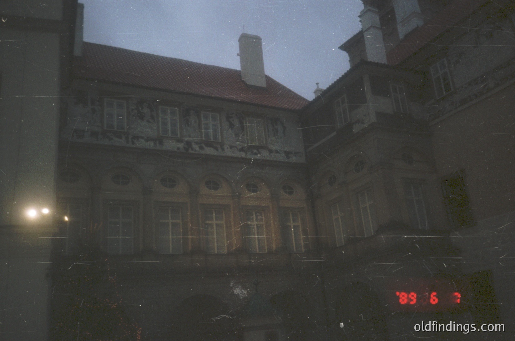Neoclassical courtyard building with intricate stone reliefs and arched windows, captured through rain-streaked glass. Date stamp "89.06.7" suggests 1989, likely Eastern Bloc-era architecture.