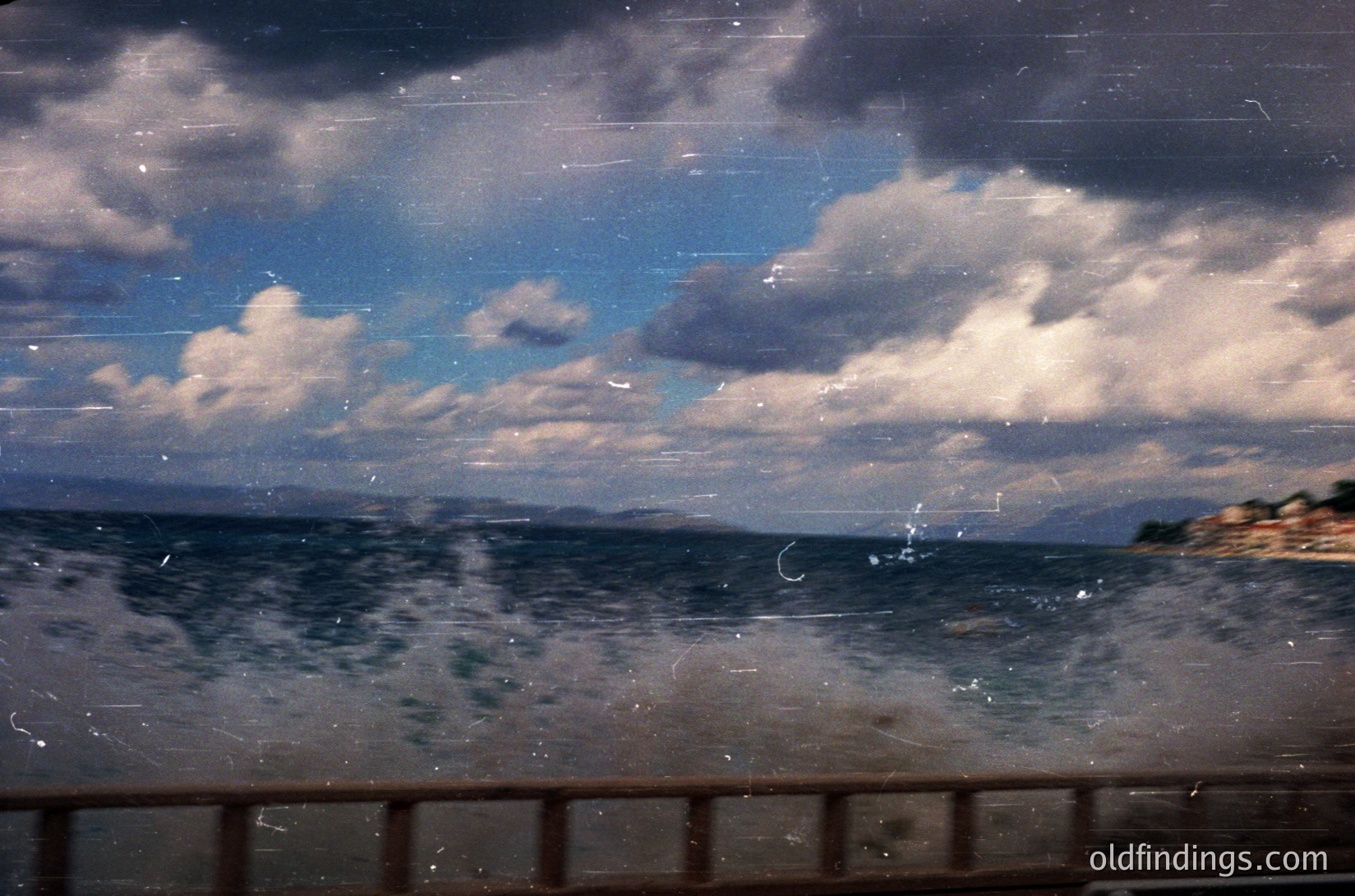Vintage seascape through aged glass, showing stormy skies and choppy waters. Distressed film grain and scratches enhance nostalgic texture. Coastal cliffs and distant landmass visible. Likely mid-20th century, monochrome or sepia-toned.