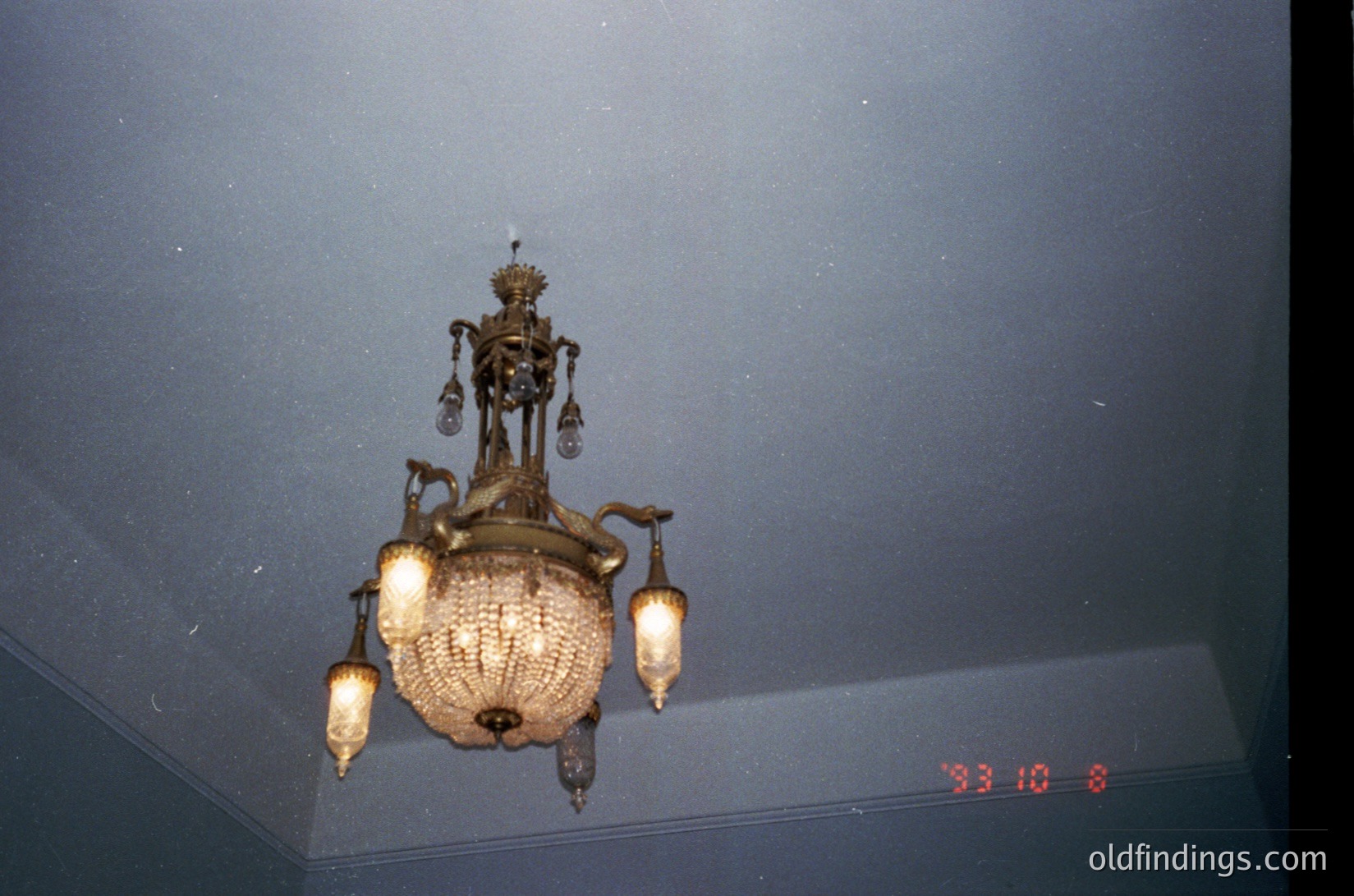 Vintage ornate chandelier with Art Nouveau-inspired metalwork and glass lanterns, mounted on a textured ceiling. Likely from a mid-20th-century European interior ( ).