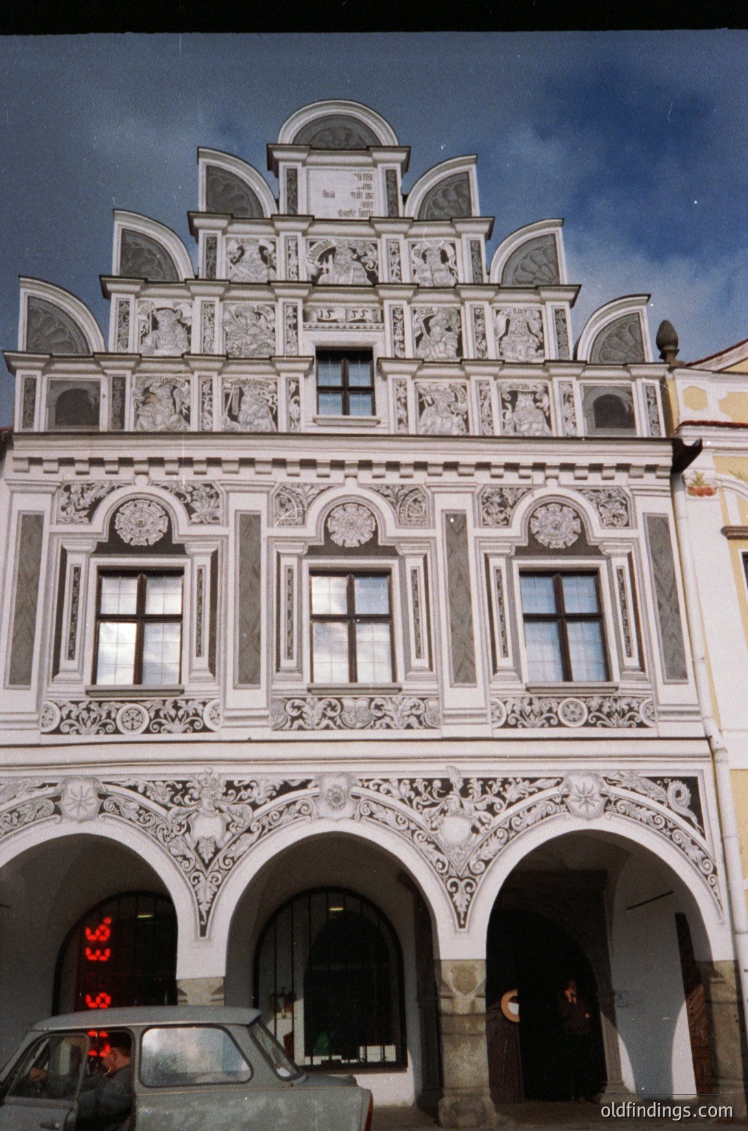 Baroque-style building façade featuring intricate stucco reliefs, arched windows, and decorative pediments. Symmetrical design with three arched ground-floor entrances. Likely European, 17th–18th century.