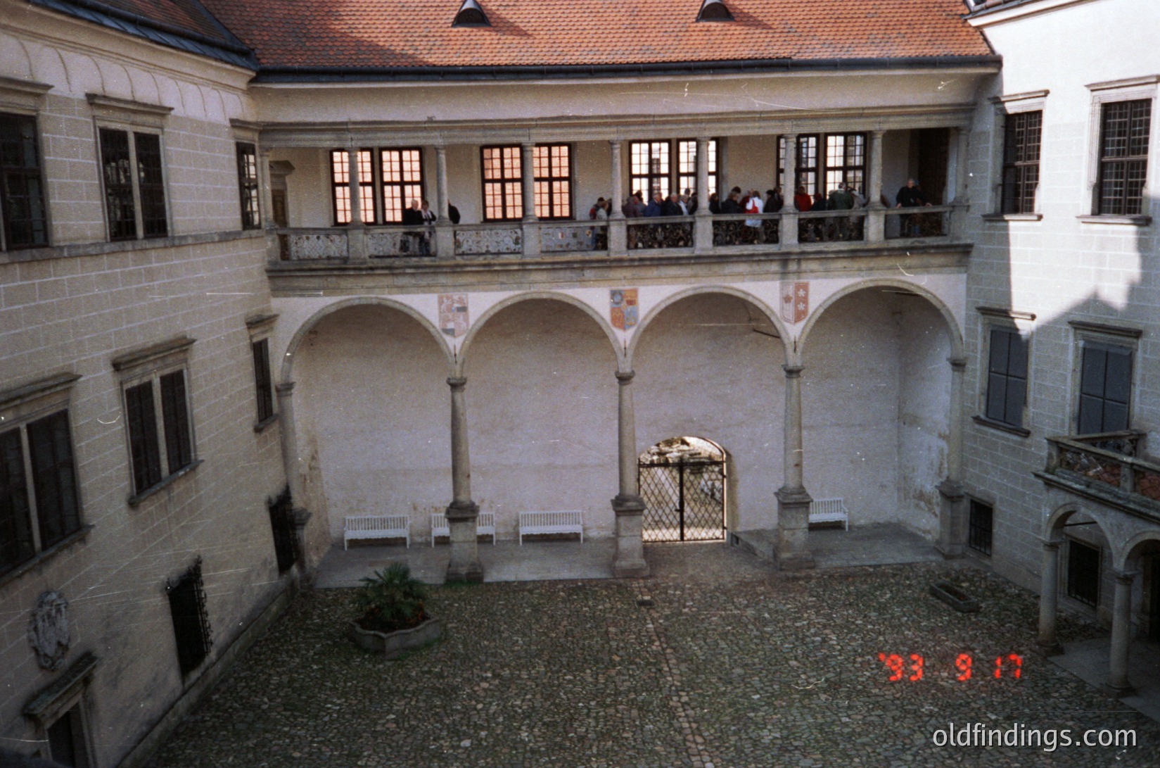 Historic courtyard with Renaissance-style arches and stone balustrades. Two-story colonnade frames a gravel-paved central area. Crowd of people on upper balcony, suggesting a public or touristic site. Date stamp "93.9.17" indicates late 1993.