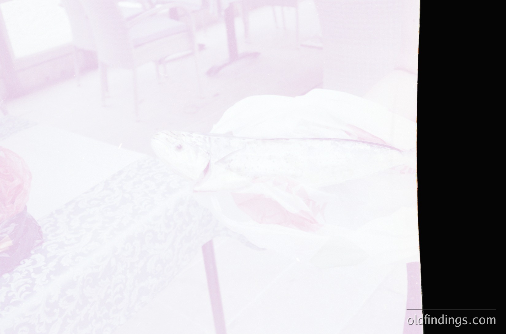 Vintage sepia-toned photo of a seated individual in a dimly lit, possibly institutional setting. The person wears a high-collared shirt and holds a pipe or cigarette holder. Background suggests a utilitarian space with blurred furniture and walls. Likely mid-20th century, possibly .