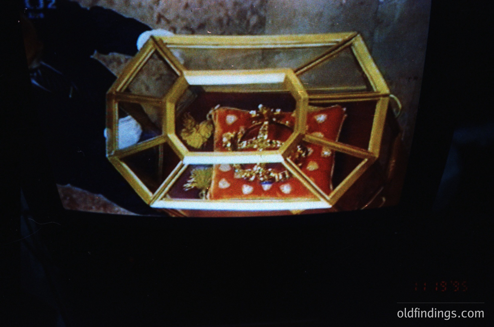 Vintage ornate jewelry display case with hexagonal gold frame, showcasing a red velvet-lined interior holding intricate gold jewelry. Likely 19th–early 20th century European craftsmanship.