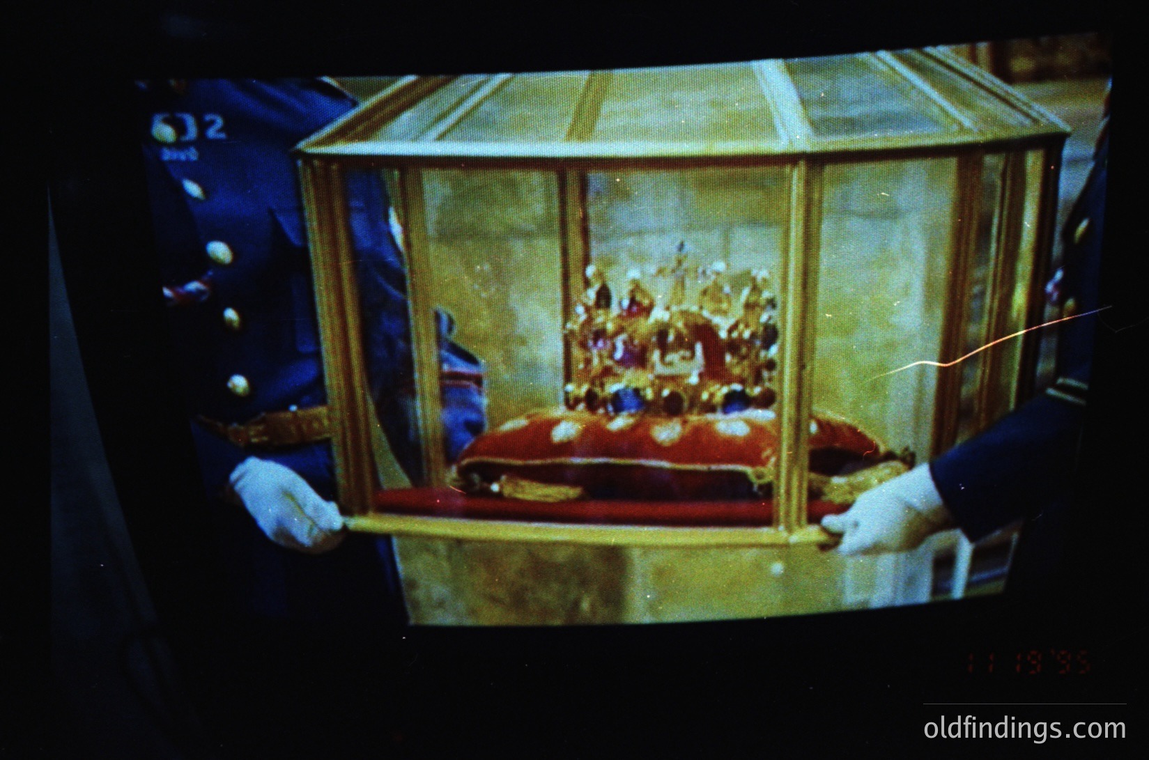 Golden ceremonial casket adorned with intricate crown and royal regalia, carried by uniformed guards in formal attire. Likely a state or coronation artifact, possibly from a European monarchy. Vintage color tone suggests mid-20th century (1950s–1970s).