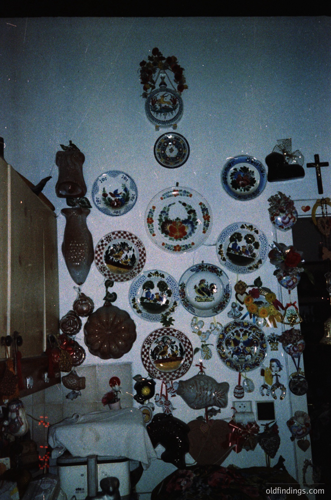 Vintage ceramic collection displayed on a light blue wall, featuring plates, vases, and decorative tiles with floral, geometric, and symbolic motifs. Likely Eastern European folk art, mid-20th century. Ideal for historical research or interior design inspiration.