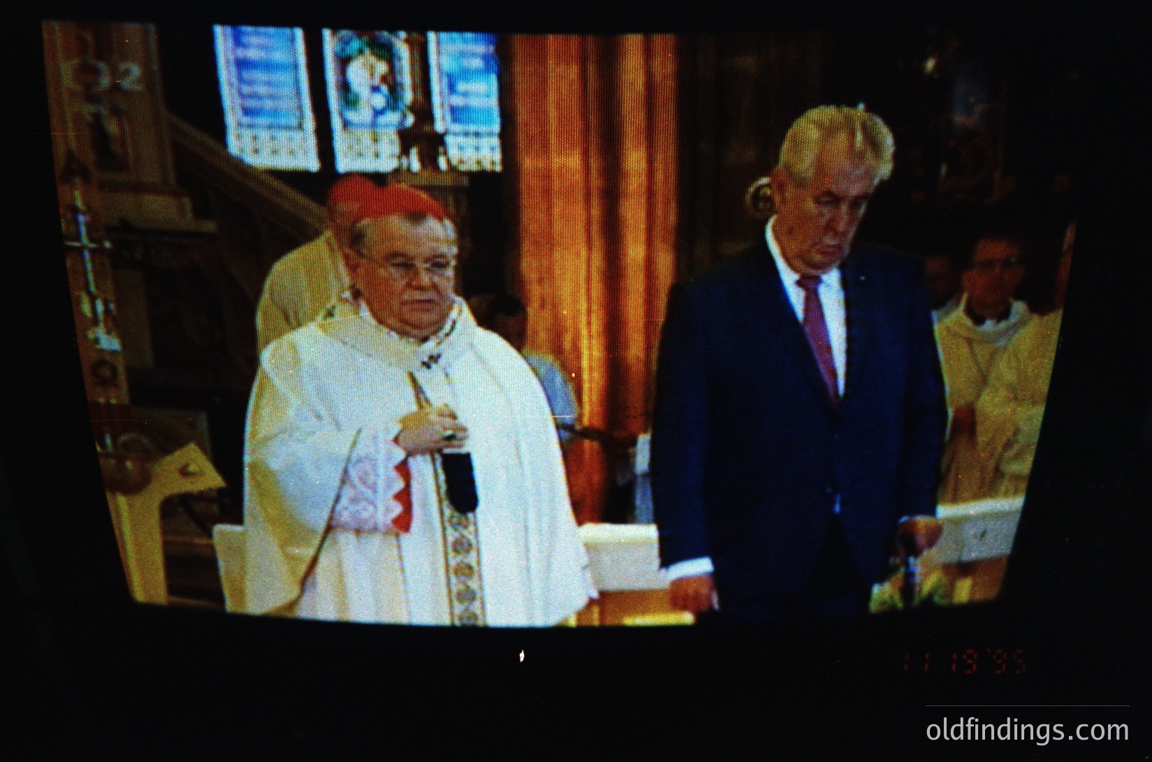 Religious ceremony featuring a cardinal in liturgical vestments conducting mass. Gothic-style church interior with stained glass windows and wooden pews. Formal attire of a secular figure in suit and tie, likely a dignitary. Mid-20th century (1950s–1970s) ecclesiastical photography.