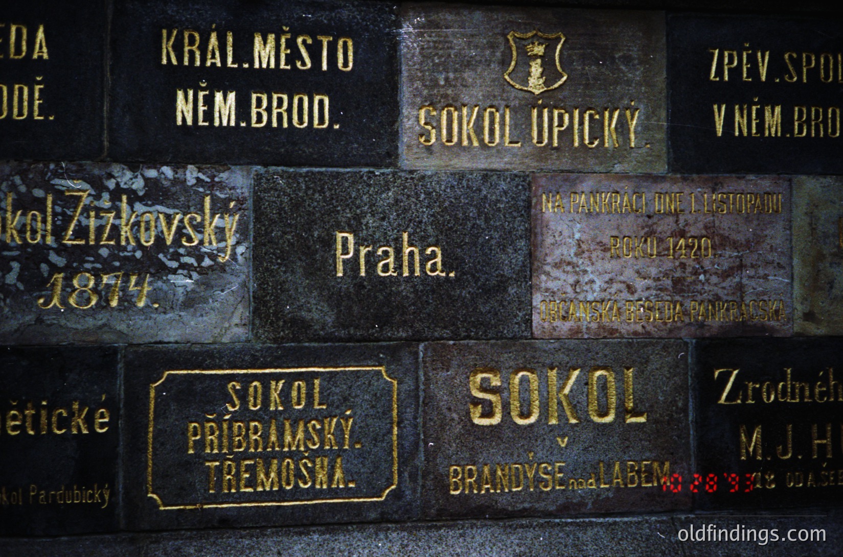 Weathered bronze plaques on a stone wall, inscribed with Czech/German text and dates. Notable entries: "Praha," "Sokol Upický," "Sokol Pribramský," and "Brandýs nad Labem" (1888). Reflects late 19th–early 20th century Czech cultural/historical societies.
