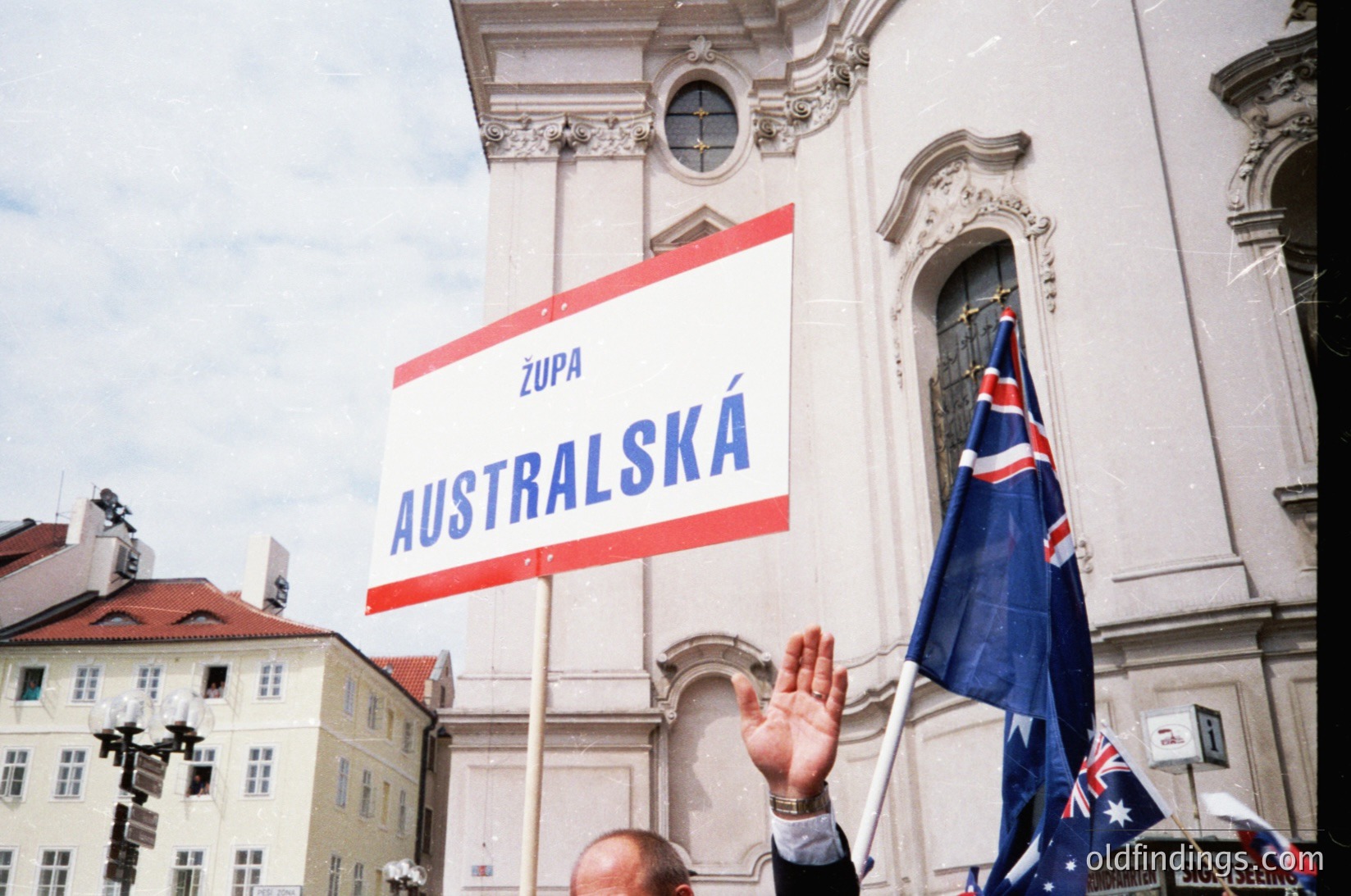 Baroque-style church façade with ornate columns and arched doorway. Crowd holding a red-and-white banner reading "Župa AUSTRALSKÁ" (Australian Parish) in Czech. Australian flag prominently displayed. Likely a cultural or religious event in Prague, Czech Republic, mid-20th century.
