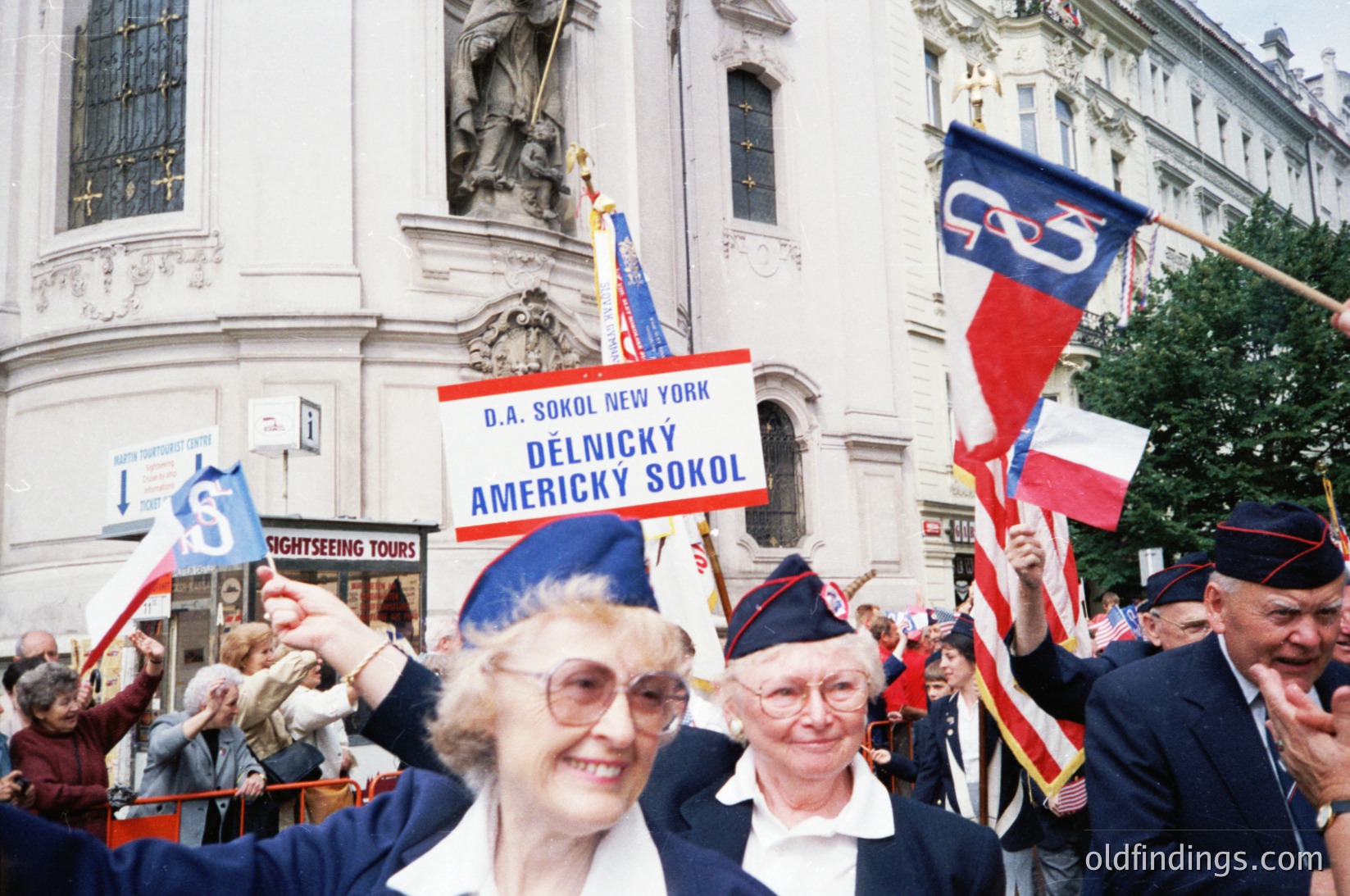 Crowd of elderly men and women in blue uniforms and red caps march in a parade, holding flags and a banner reading "D.A. Sokol New York" and "Delnicky Americky Sokol." The event appears to be a cultural or heritage celebration, likely in New York City, during the late 20th century. #