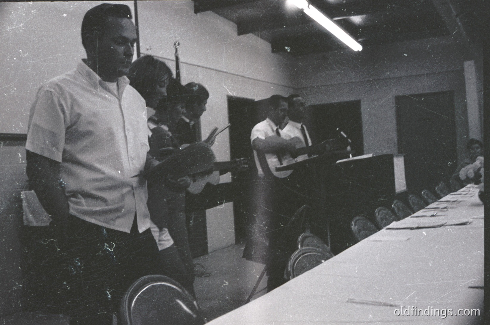 Black-and-white photo of a 1960s–1970s conference or meeting. Three individuals at a long table with microphones, suggesting a panel discussion or lecture. Attendees seated in rows, facing forward. Fluorescent lighting and basic institutional decor indicate a formal indoor venue. Potential historical context: civil rights, education, or public policy discussions.