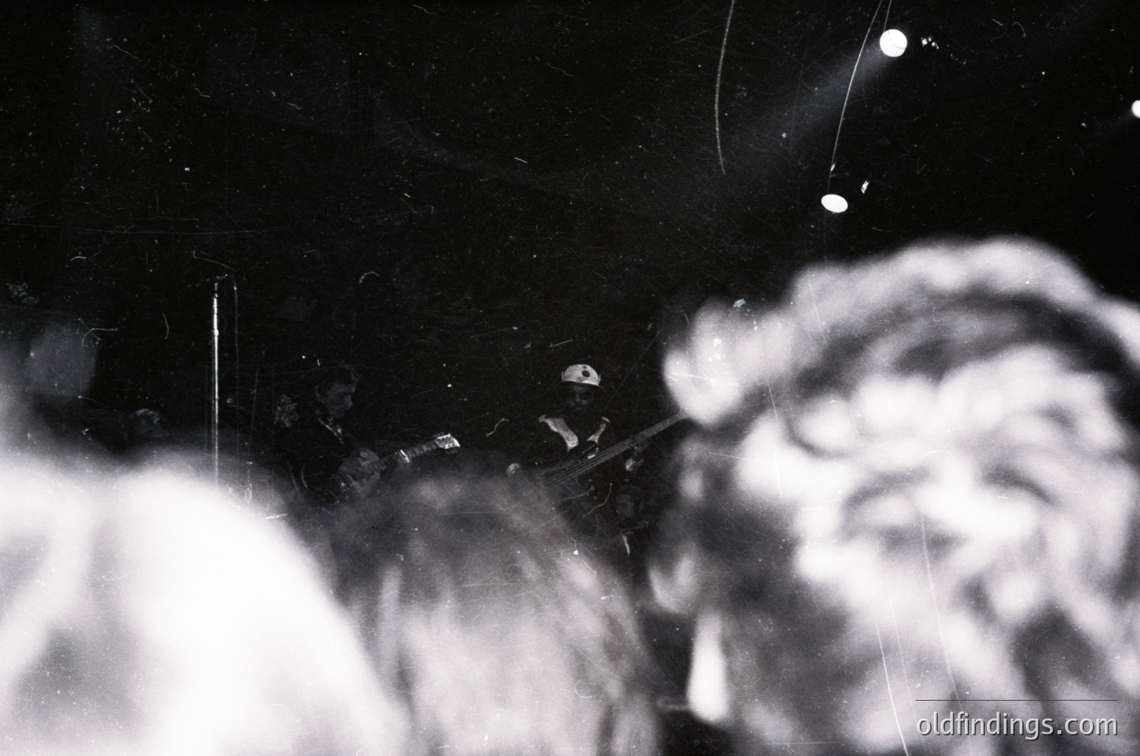 Vintage black-and-white photo of a close-up nighttime scene featuring a blurred, illuminated face and a cigarette held between fingers. Light trails from camera shutter speed or motion blur. Likely 1940s–1960s, urban setting.