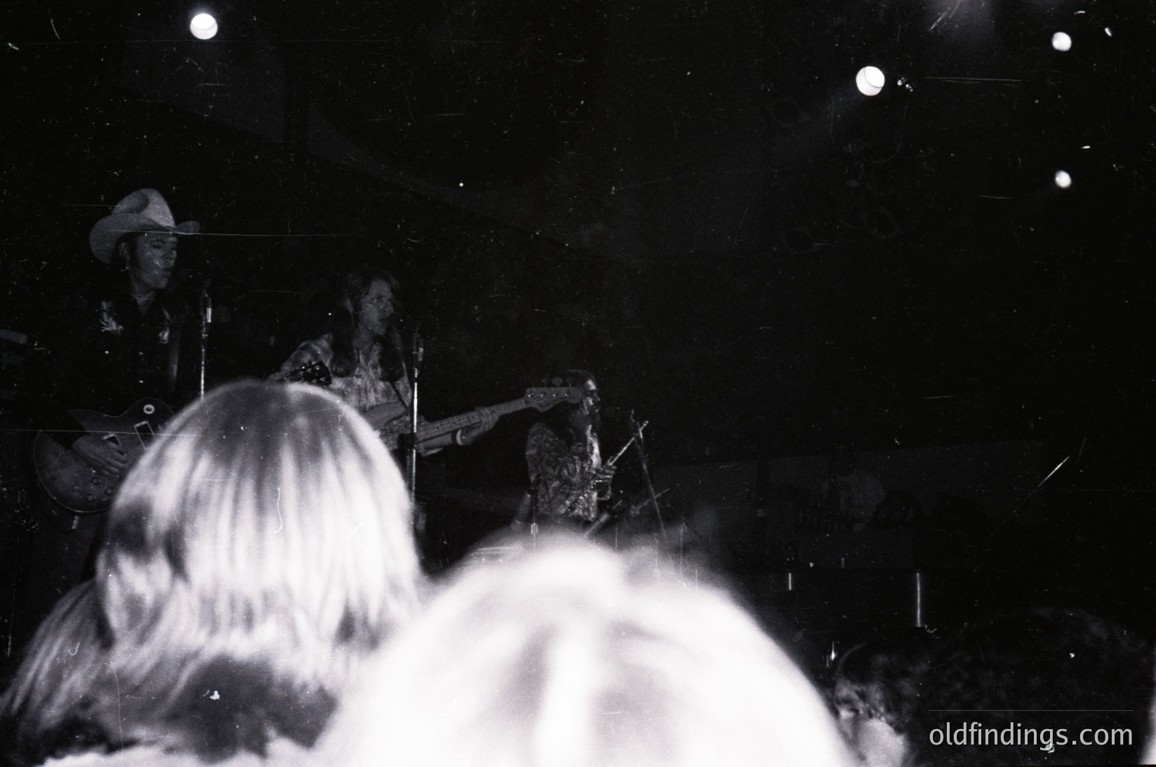 Black-and-white shot of a live jazz performance in a dimly lit venue. Backlit saxophonist playing center stage, with blurred audience silhouettes in foreground. Art Deco lighting fixtures and bokeh effects enhance ambiance. Likely mid-20th century () in a North American urban setting (, ).