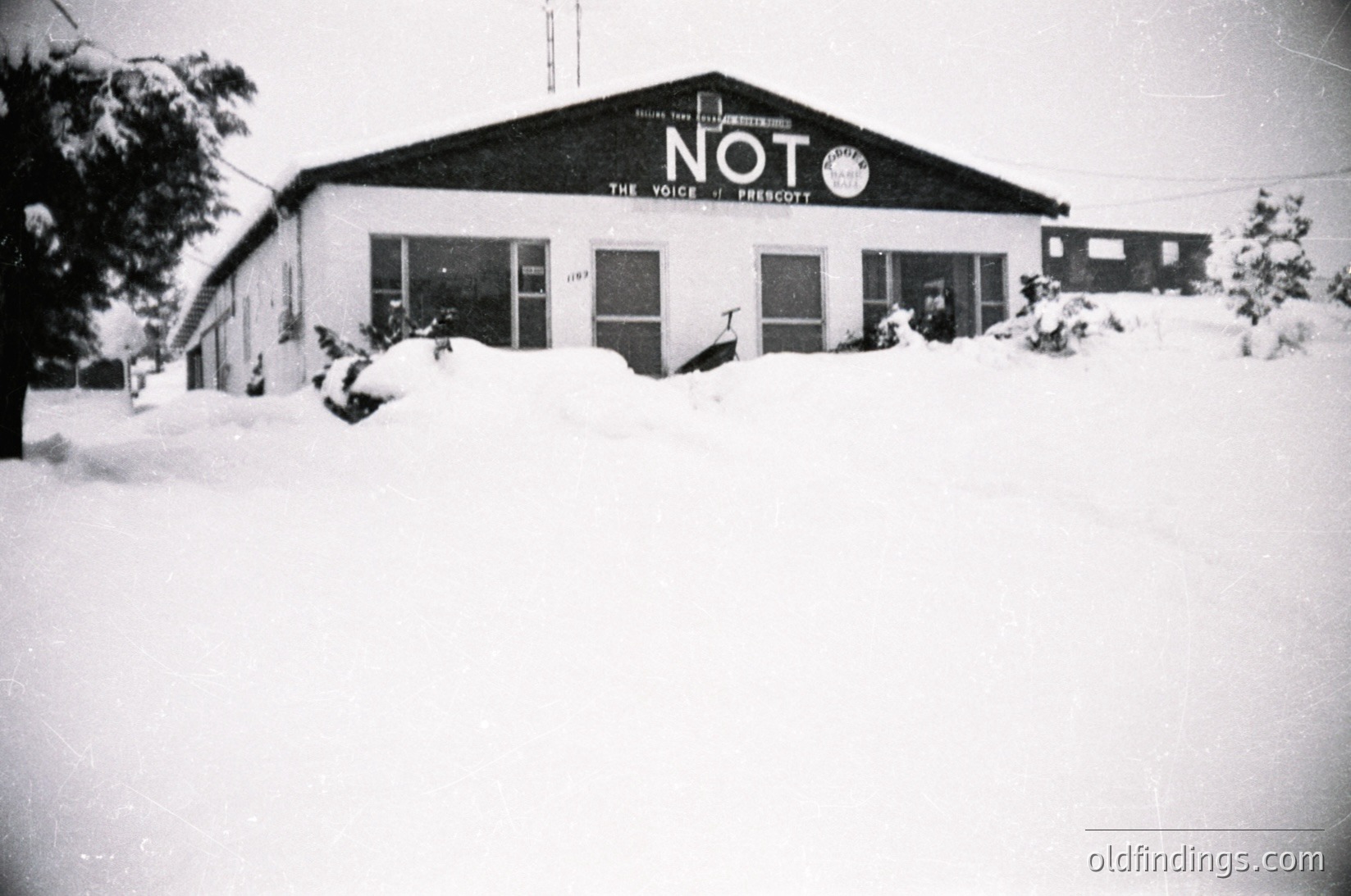 Mid-century brick building blanketed in snow, featuring bold signage: "NOT THE VOICE OF FRESNO." Single-story with large windows, likely a community center or radio station. Snow-covered landscape suggests winter 1950s–1970s, USA.