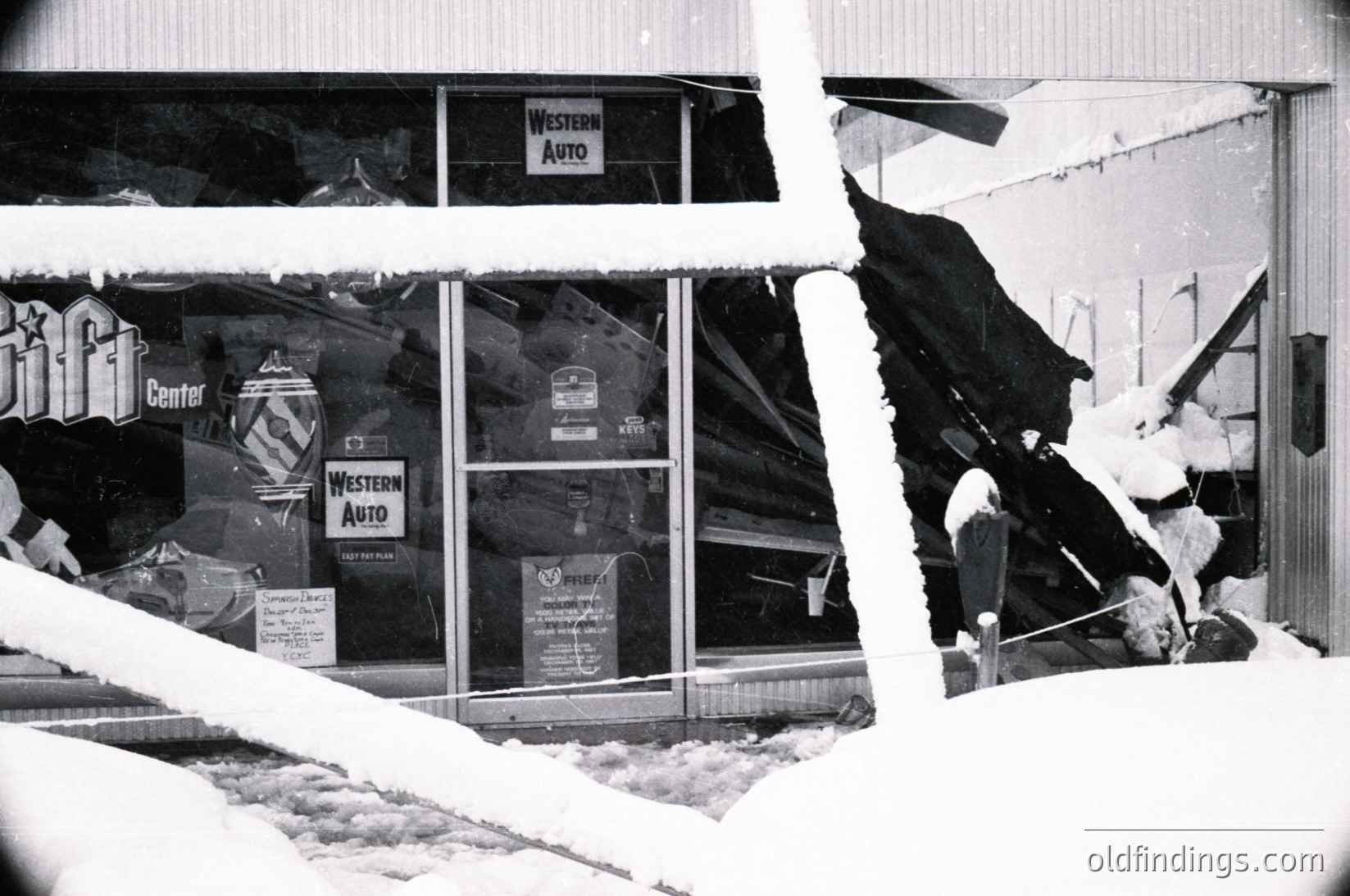 Snow-damaged storefront with "Western Auto" signage and shattered glass, likely mid-20th century. Visible branding includes "Pfizer" and "Pillsbury" ads. Structural damage suggests severe winter storm impact.