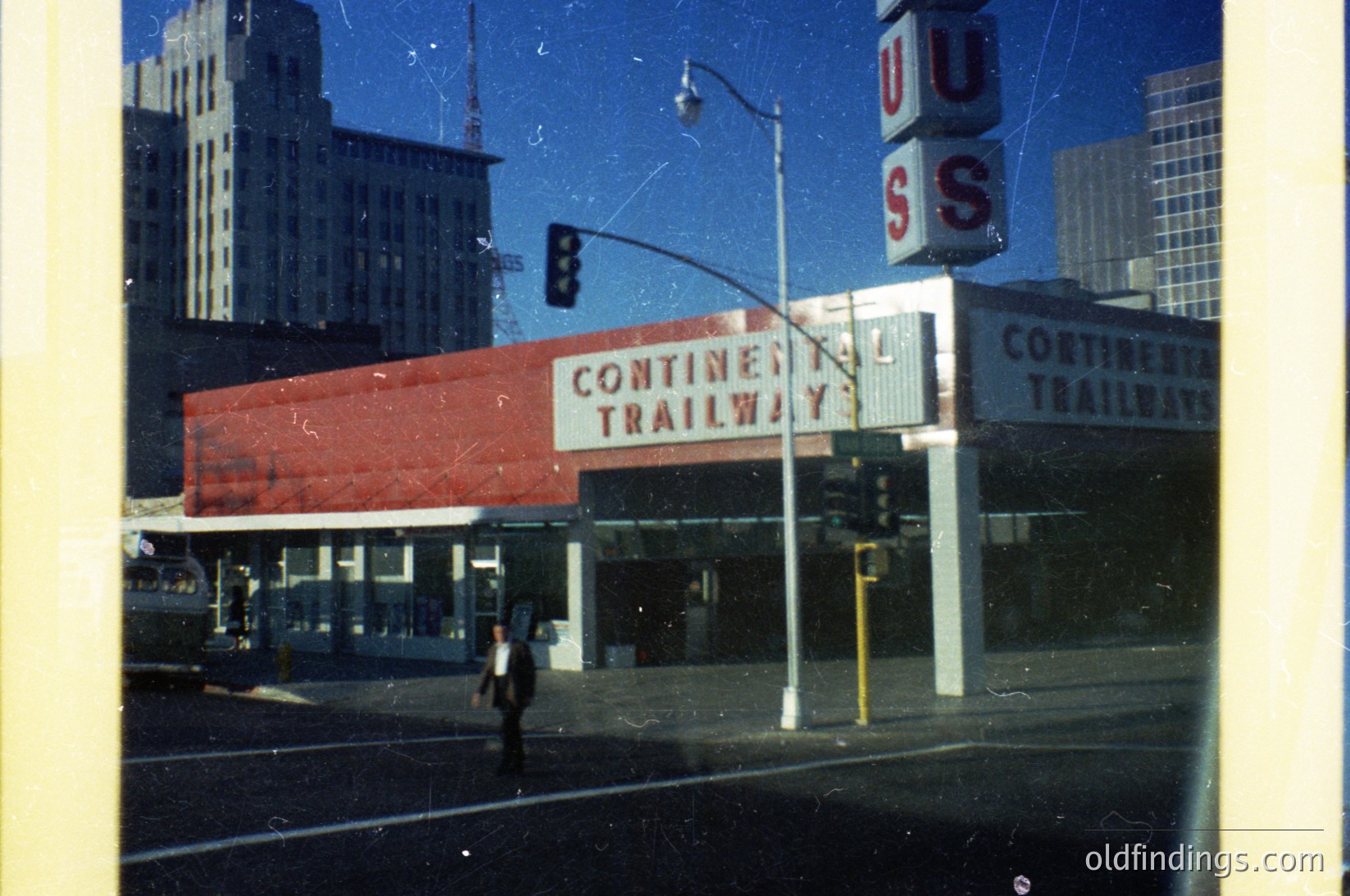 Vintage urban scene featuring a **Continental Trailways bus station** with bold red signage and "USS" neon sign. Mid-century architecture with Art Deco influences. Pedestrian crossing street near high-rise buildings, suggesting a major city hub. Likely **1950s–1960s** era.