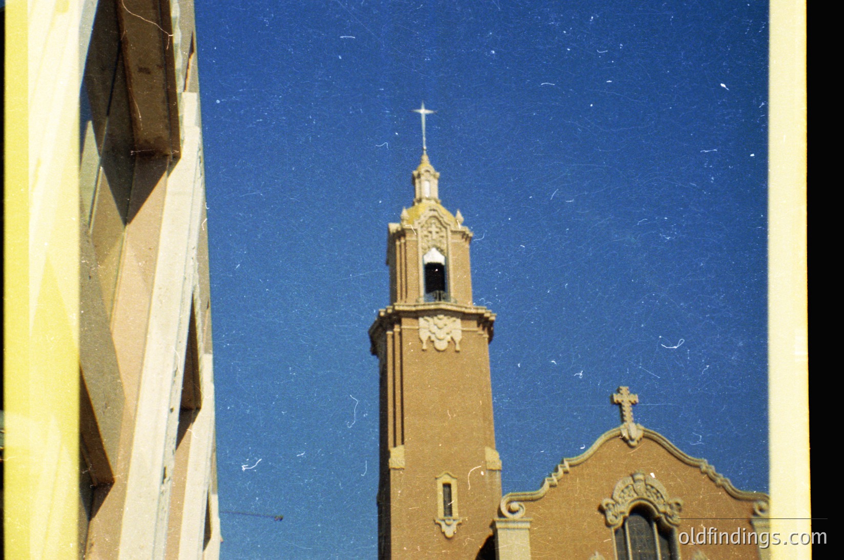 Vintage sepia-toned photo of a brick church with a square bell tower topped by a golden cross, framed by a geometric structure. Architectural details include arched windows and decorative stonework. Likely Eastern European, 20th-century religious architecture.
