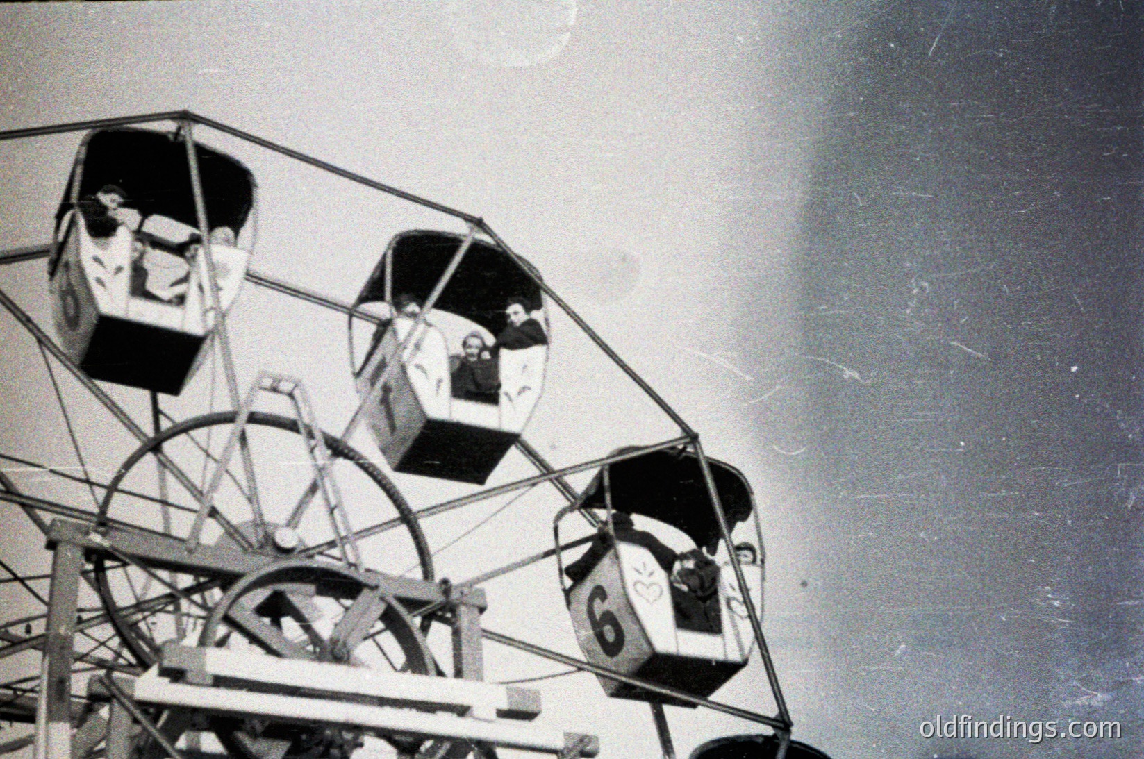 Vintage amusement park swing ride with enclosed gondolas, numbered "6" visible. Two people seated, mid-ride, against a blurred sky. Structural metal framework and curved arm design suggest mid-20th century construction. Ideal for historical amusement park research or nostalgic design references.