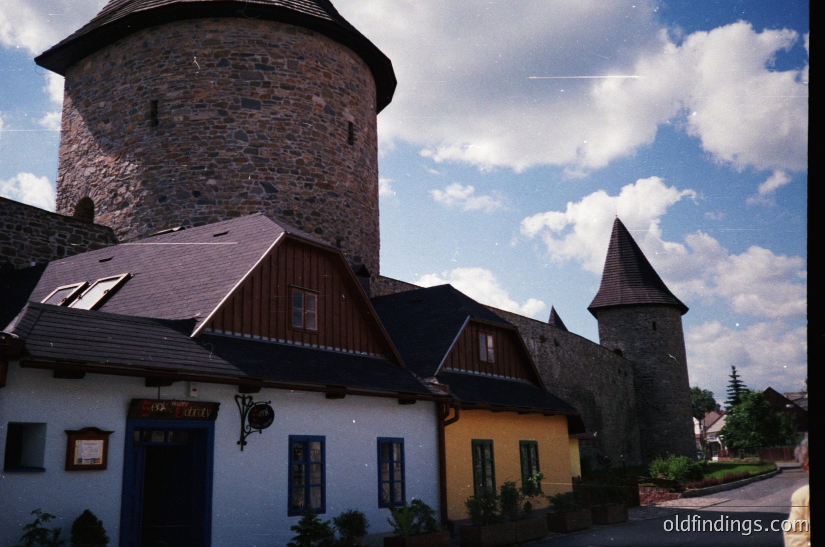 Medieval stone tower with conical roof flanked by colorful 19th-century homes ( )