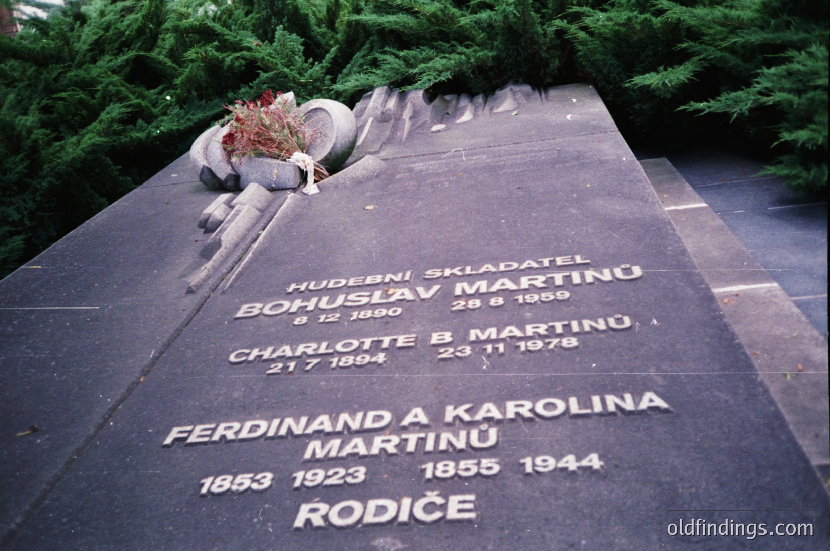 Monumental gravestone in a cemetery with engraved names and dates in Czech/Slovak script. Bohuslav Martinů (composer, 1890–1959), Charlotte B. Martinů (1884–1978), Ferdinand & Karolina Martinů (1853–1923 & 1855–1944). Decorated with a wreath and pine branches.