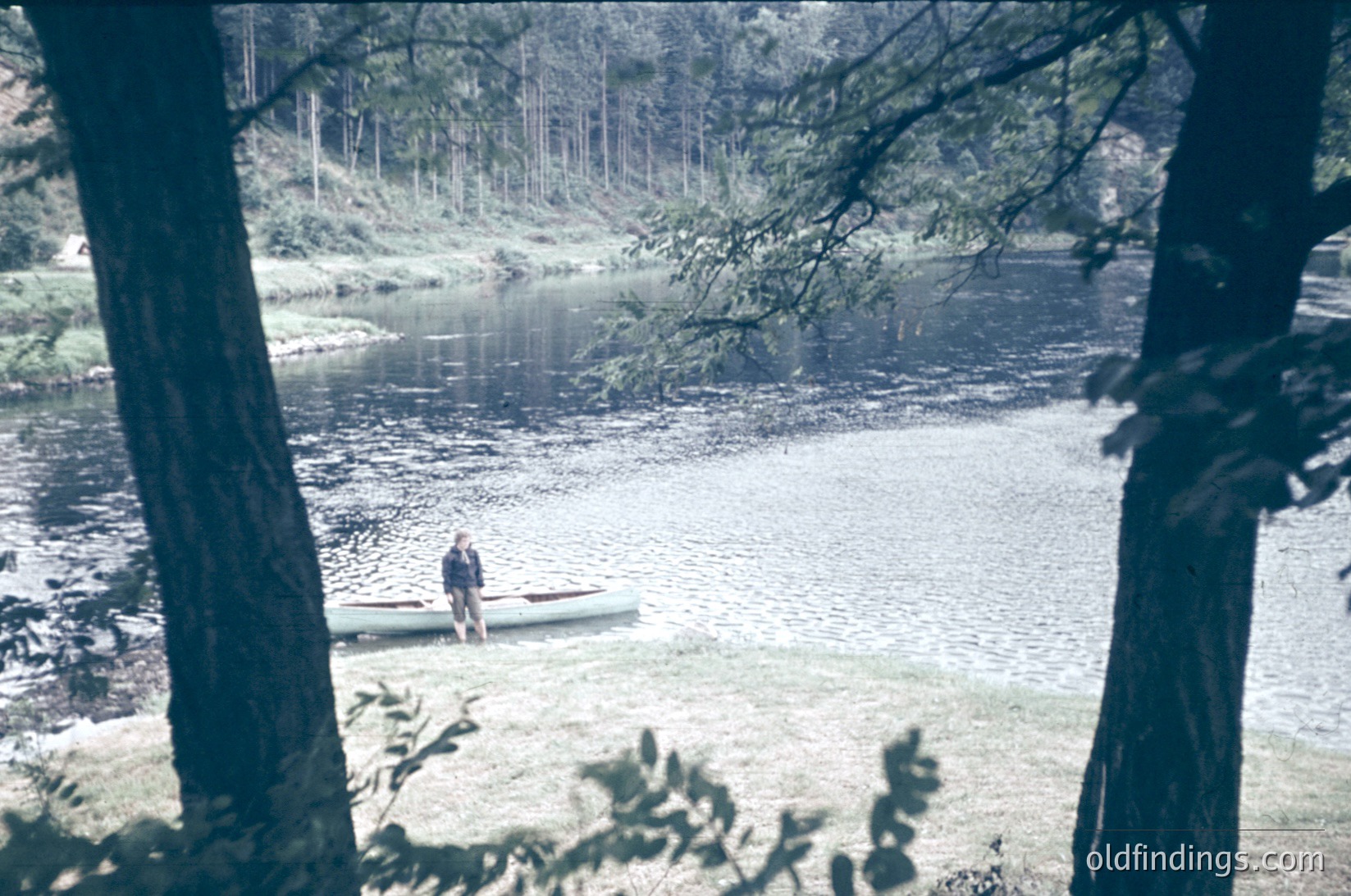 Vintage sepia-toned photo of a lone individual in a canoe on a calm river surrounded by dense forest. The scene evokes mid-20th century outdoor recreation, likely or . Ideal for nature, adventure, and historical stock imagery.