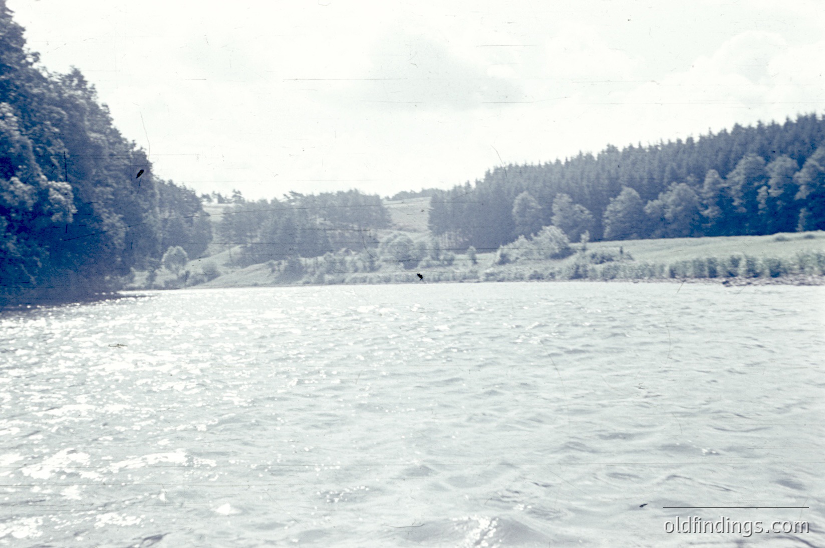 Frozen lake bordered by snow-laden forest and open fields under overcast skies. *(Note: The sepia tone suggests potential vintage quality, likely mid-20th century.)*