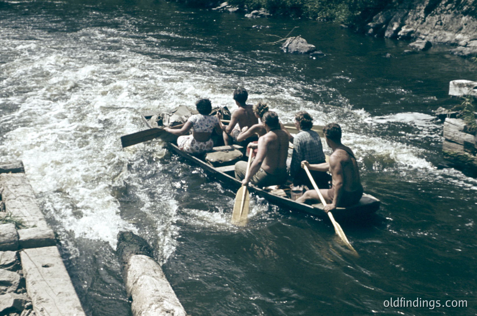 Six men in traditional wooden rowboats navigate turbulent waters, likely a river or rapid. Mid-20th century attire suggests or outdoor recreation. Scenic mountainous backdrop hints at a remote or wilderness location.