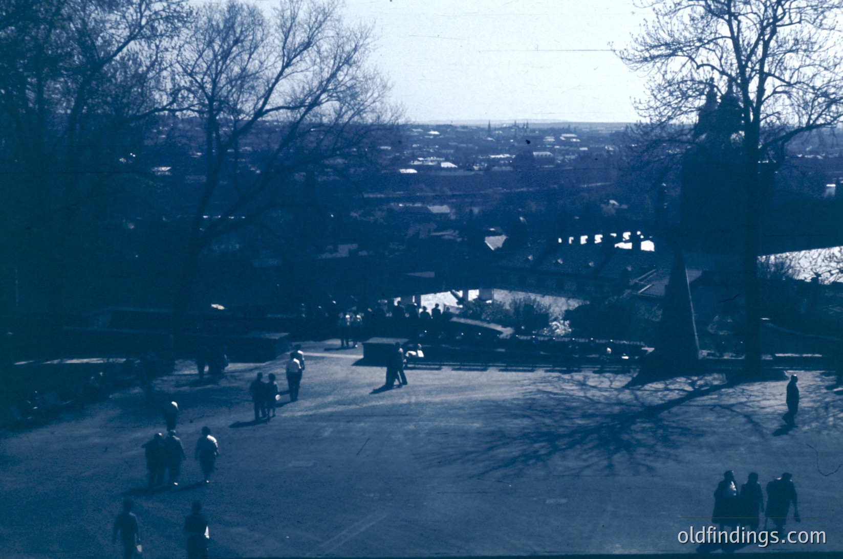Vintage sepia-toned aerial view of a park with sparse crowds, likely 1960s–1970s. Open plaza with leafless trees, a central fountain, and distant urban sprawl. Architectural elements include low-rise buildings and a bridge. Ideal for urban planning, historical research, or nostalgic design references.