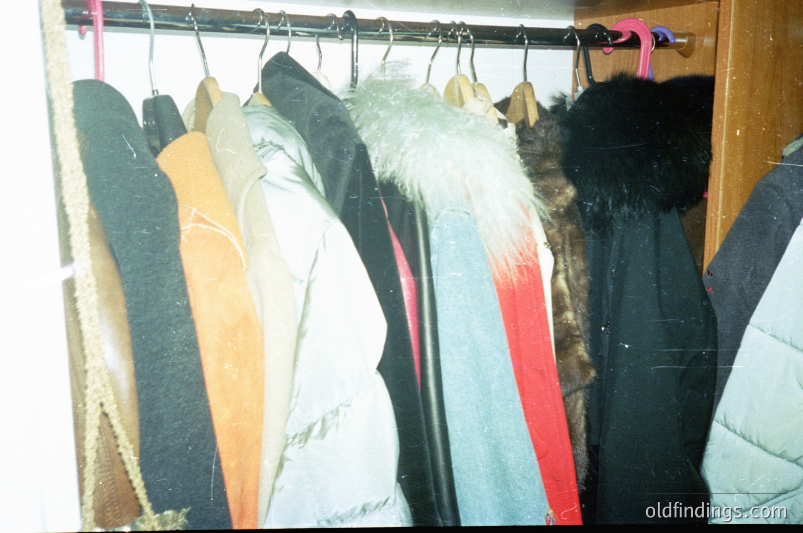 Vintage winter clothing rack featuring fur-lined coats, wool jackets, and synthetic parkas. Hanging hooks show signs of wear, suggesting long-term use. Interior setting likely residential or small storage space. Potential 1970s–1990s era based on fabric styles and lighting.