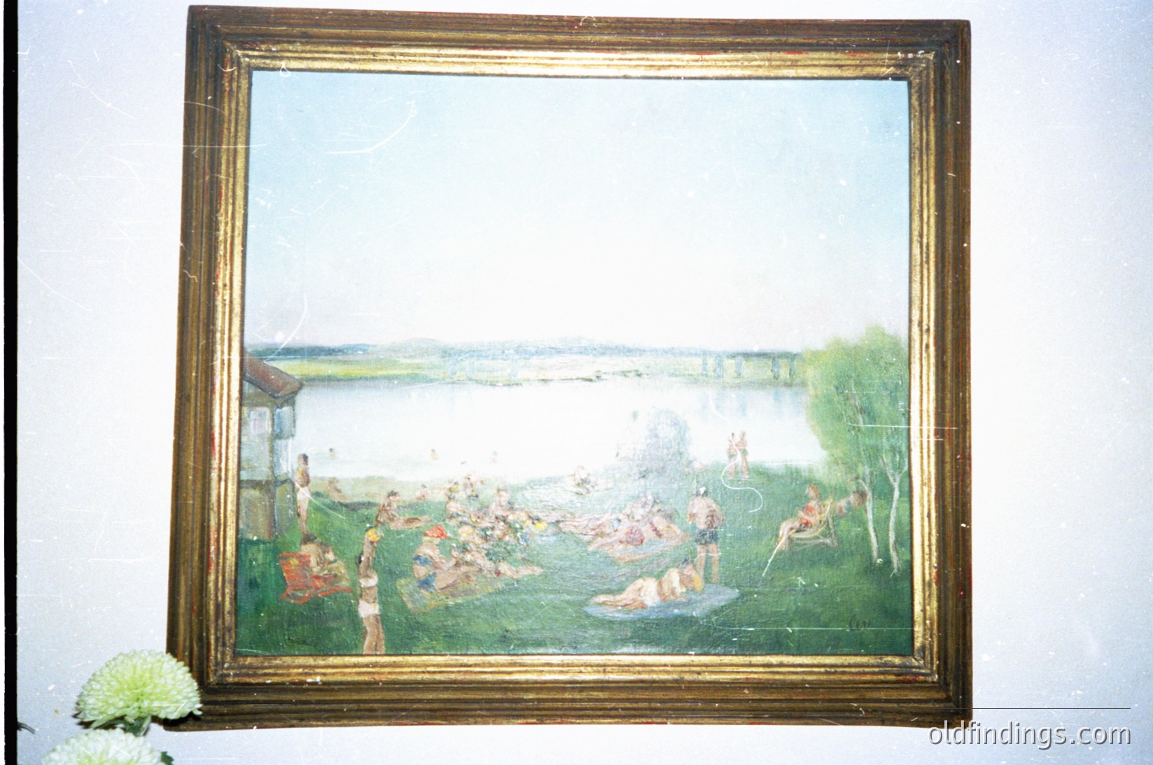 Vintage impressionistic painting depicting a lakeside gathering, likely late 19th to early 20th century. Golden frame with visible wear, set against a neutral wall. Scene includes figures in period attire, boats on water, and lush greenery. Evokes leisure culture of the era.