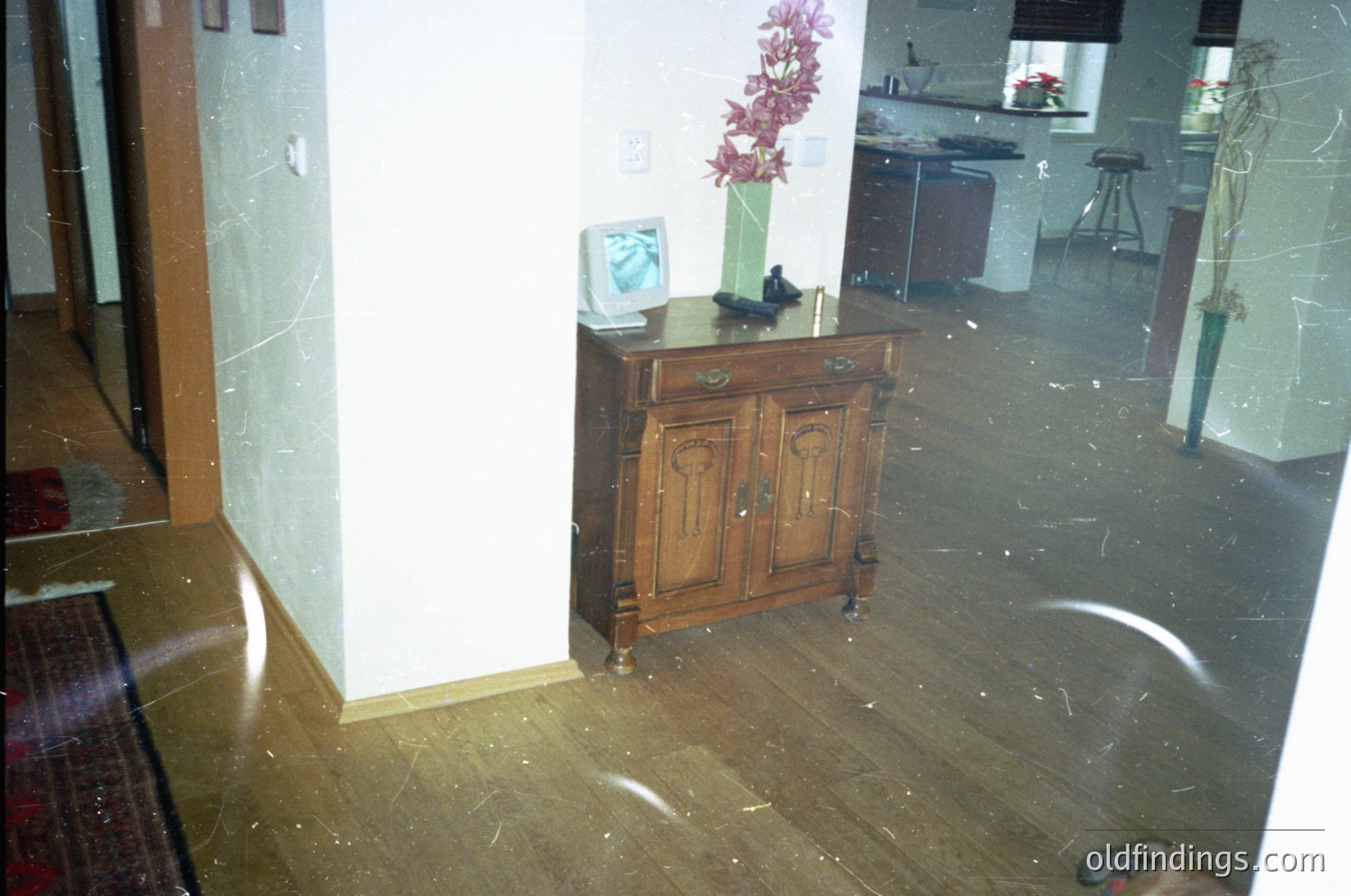 Vintage wooden sideboard in a flooded interior, submerged in water up to mid-calf height. Marble walls and tiled floor show water damage. Decorative vase and framed photo visible above waterline. Likely residential damage from plumbing failure.