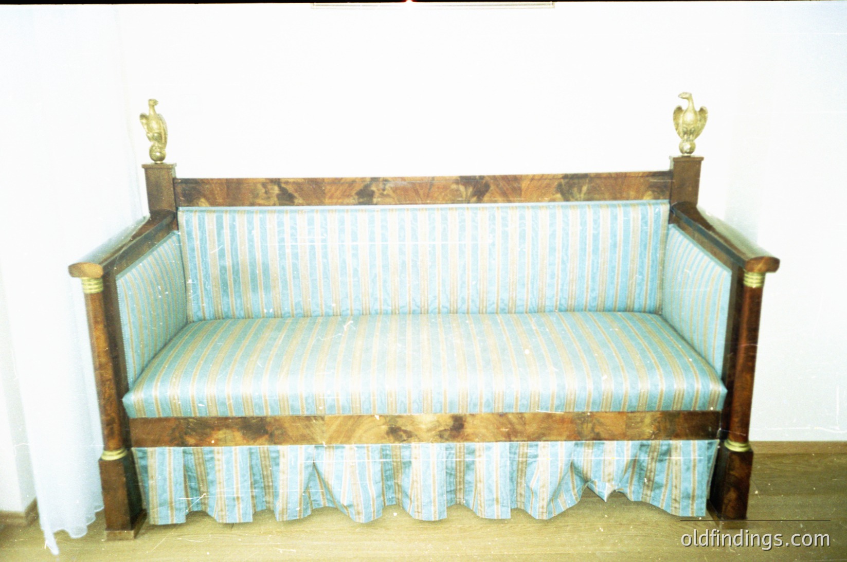 Antique wooden bench with ornate brass eagle finials, upholstered in vintage striped fabric. Dark wood grain and aged patina suggest 19th-century craftsmanship. Ideal for historical interiors, vintage decor, or museum displays.