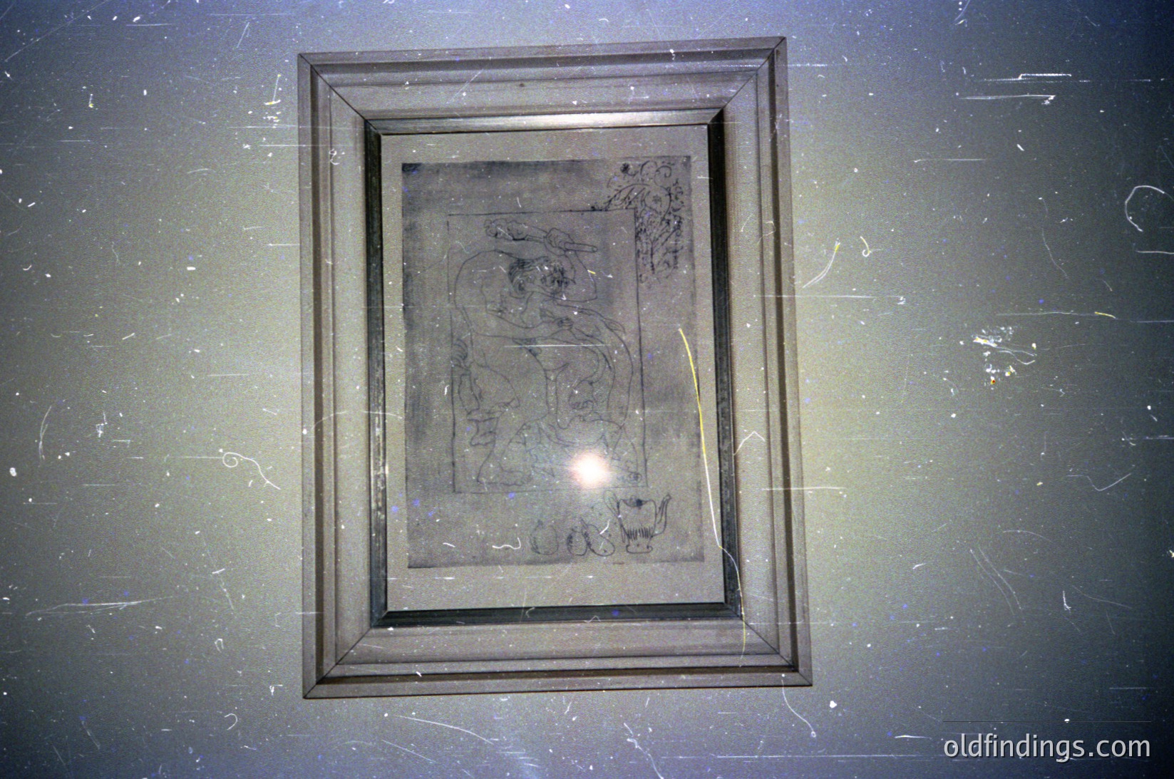 Vintage framed parchment or paper with faded, hand-drawn or engraved geometric and symbolic designs, possibly religious or ceremonial. Darkened edges suggest age and exposure to light. Mounted on a textured wall, likely in a museum or archive setting.