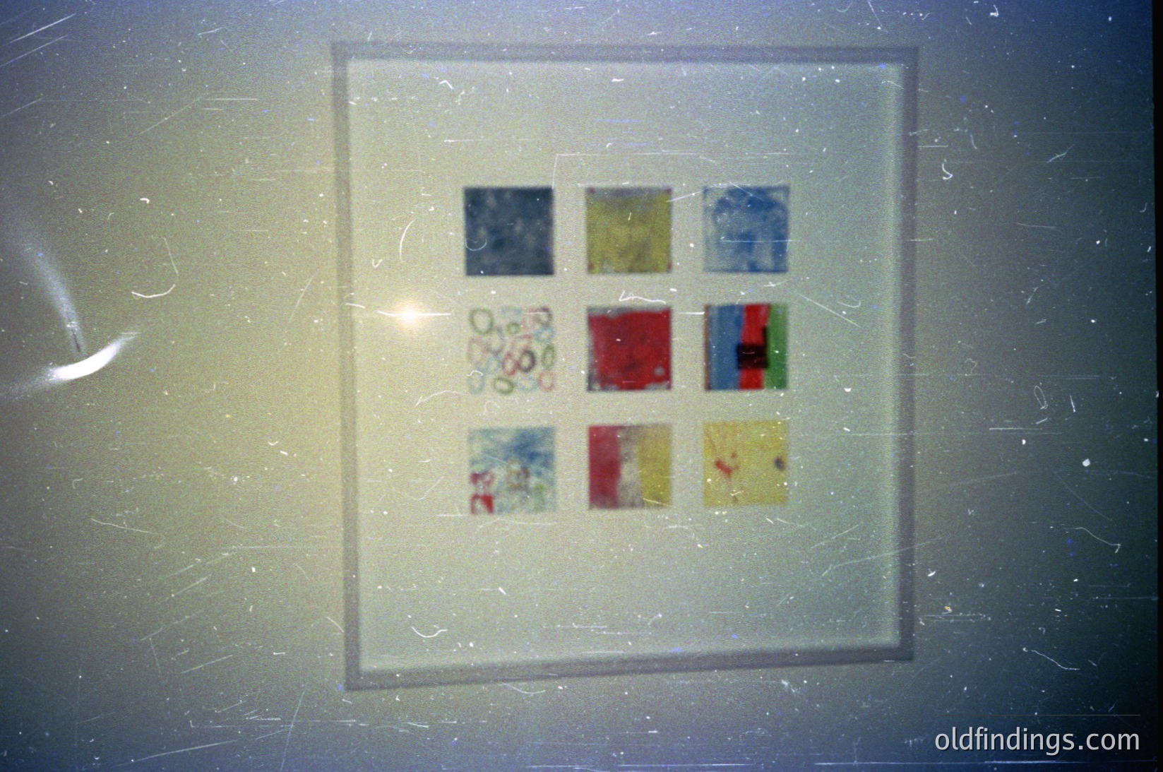 Vintage 35mm slide frame featuring nine small, faded color patches—likely test strips or artistic samples. Patterns include floral, geometric, and solid hues (red, blue, green, yellow). Possible 1960s–1980s photography reference.