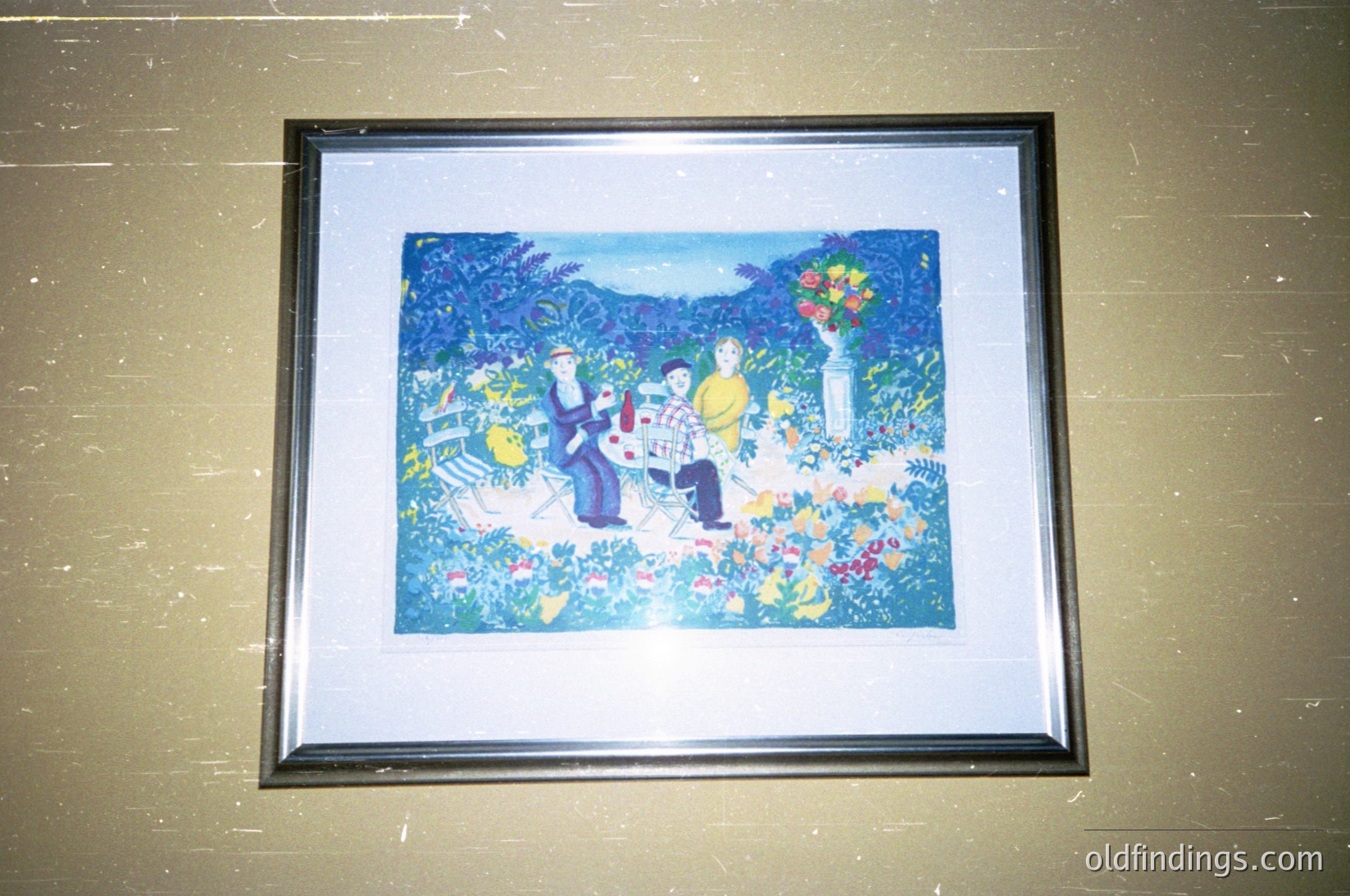 Vibrant folk-art painting depicting three figures seated under a blooming tree in a lush garden. Bold, stylized floral motifs and bright blues/greens dominate the composition. Style suggests Eastern European folk art, likely from the 20th century.