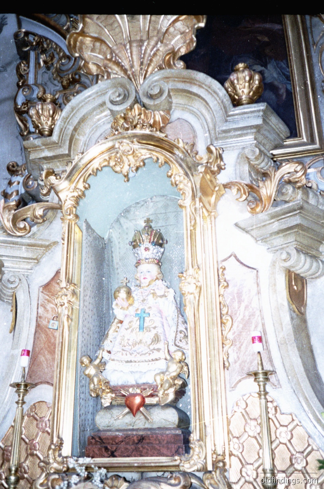 Baroque-style religious altar featuring a gilded statue of the Virgin Mary with Child, crowned and holding a cross. Ornate frame includes cherubic figures, floral motifs, and candle holders. Likely European, 17th–18th century.