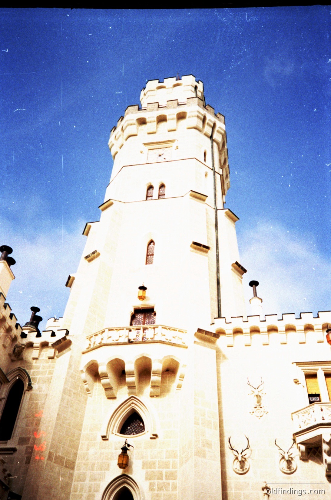 Gothic-style tower with crenellated parapets, arched windows, and decorative deer antlers flanking the entrance. Lighting suggests vintage film grain, likely –. Architectural details evoke European castle influence.