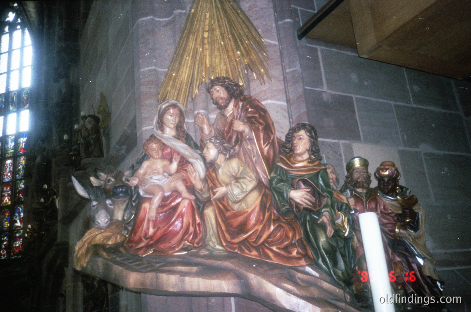 Baroque-style religious altarpiece depicting the Nativity scene: central figures of Mary, Joseph, and infant Jesus with gold halo, flanked by kneeling shepherds and a standing angel. Intricate gilded details and rich drapery. Stone church interior with stained-glass windows in background. Likely European, 17th–18th century.