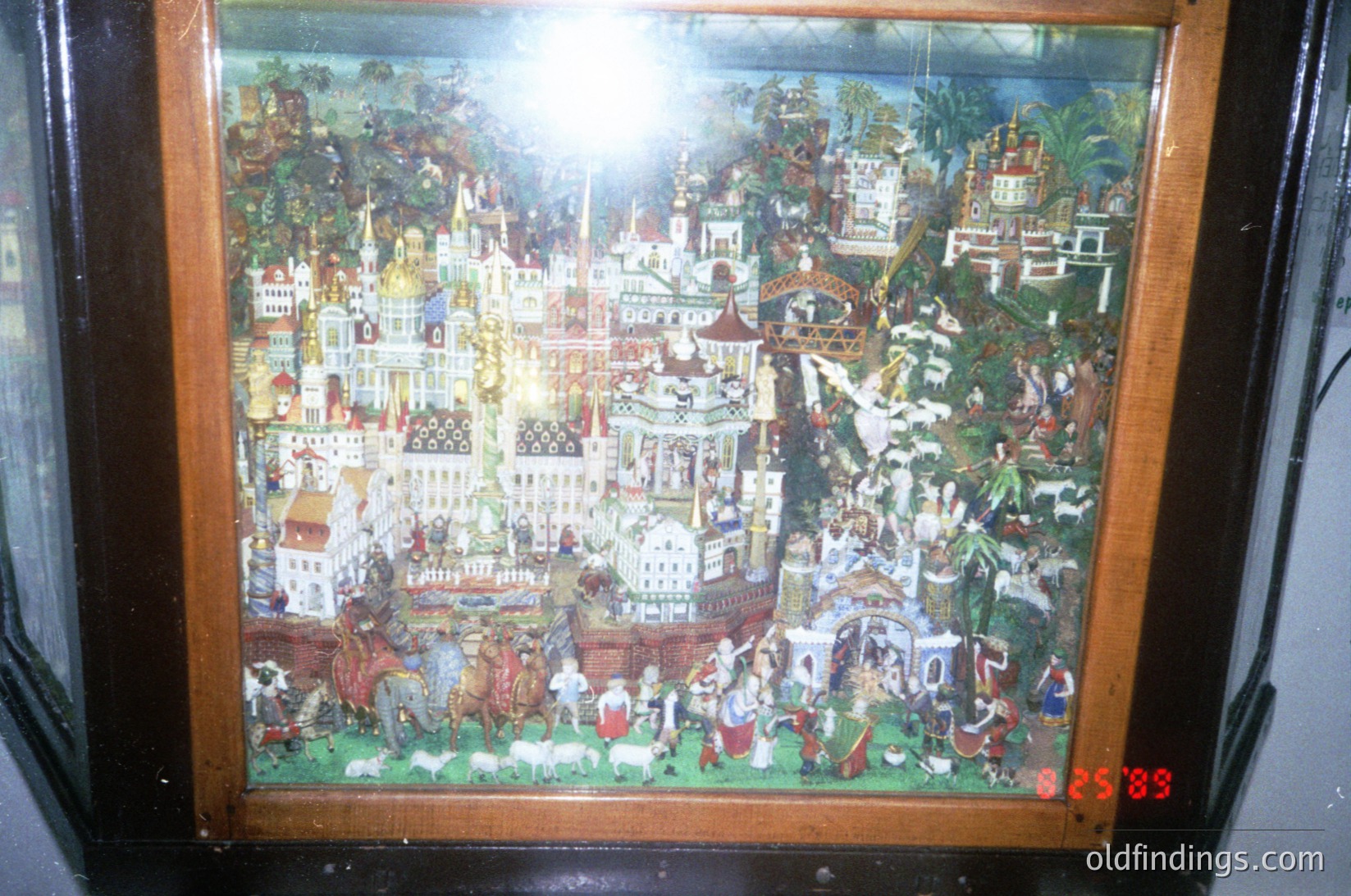Vintage painted scene depicting a bustling medieval European town with ornate architecture, including spires, domes, and a central castle. Figures in period attire engage in daily activities—farming, trade, and procession—set against lush, detailed greenery. Likely 19th-century folk art, possibly Eastern European.