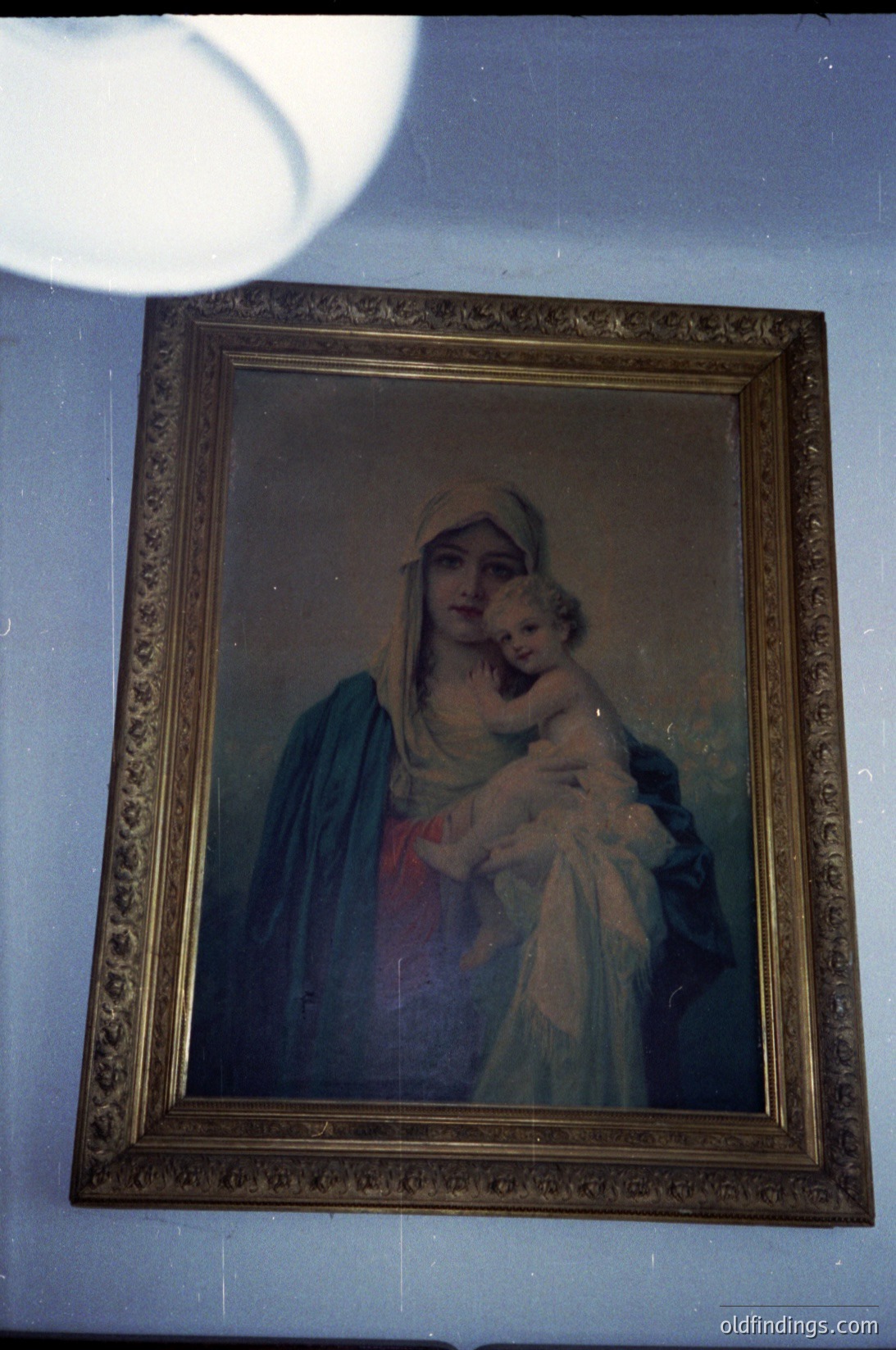 Vintage religious portrait depicting the Virgin Mary cradling Christ Child in ornate gold frame, likely 19th–early 20th century. Soft color palette with muted blues, reds, and gold accents. Ideal for historical art collections or religious iconography research.