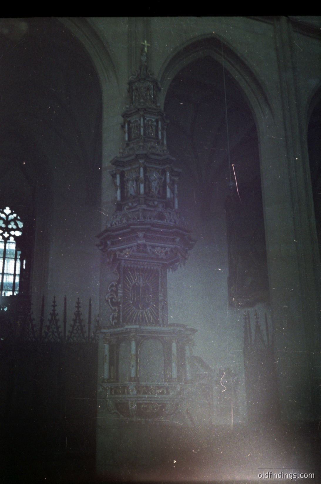 Vintage sepia-toned photograph of an ornate Gothic-style pulpit inside a church, featuring intricate carvings and a central sunburst motif. Gothic arches and stained-glass windows visible in background. Likely European, mid-20th century.