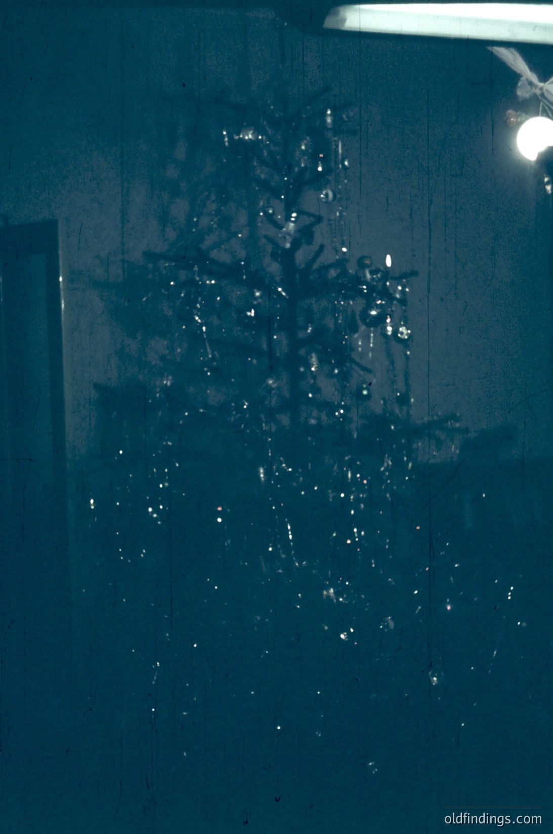 Vintage Christmas tree reflection in a frosted glass door, showcasing intricate ornaments and twinkling lights. Warm indoor glow contrasts with cold exterior. --- *Note: Style and lighting suggest mid-20th century (likely 1960s–1970s) for commercial/archival use.*