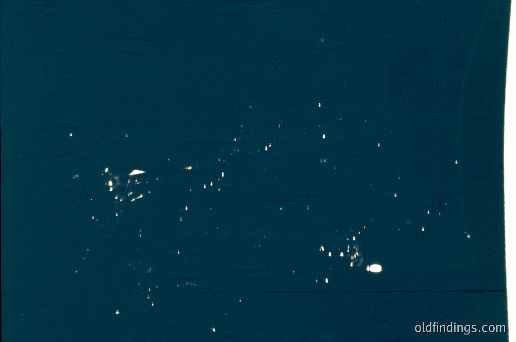 Vintage black-and-white aerial photo of scattered ice crystals on a dark surface, likely a window or glass pane. Composition suggests low-light conditions, possibly nighttime or overcast skies.