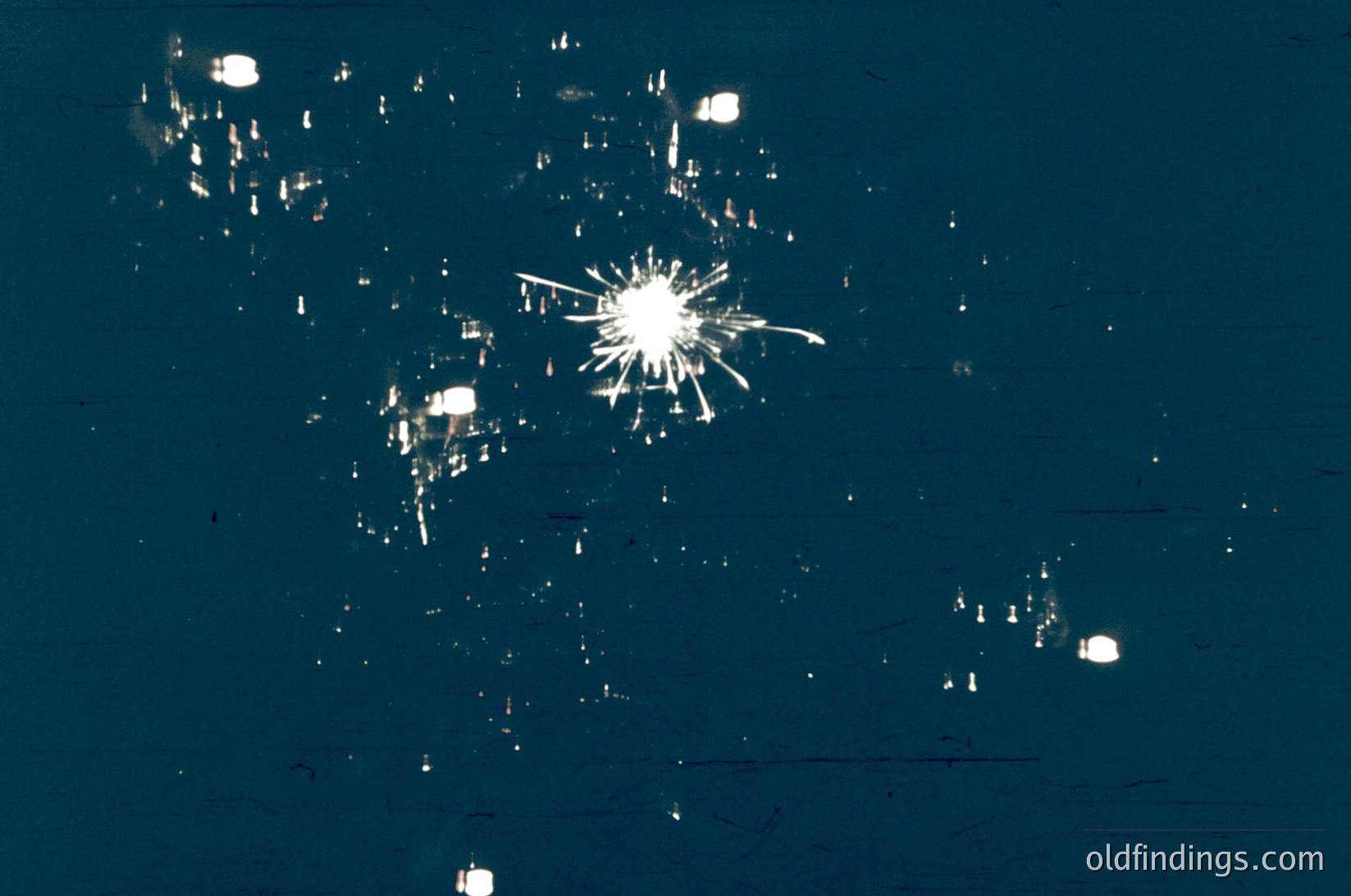 Close-up of shattered glass fragments on a dark surface, likely from a broken window. Radial cracks radiate from a central impact point, with smaller debris scattered around.