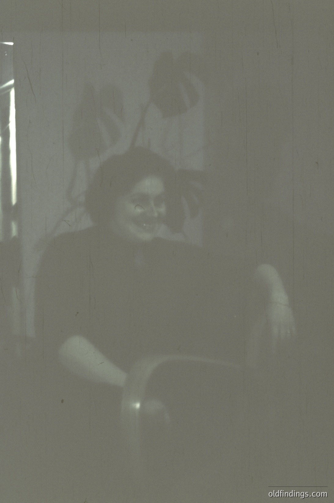 Vintage projection of a blurred silhouette of a seated person against a light source, likely from a slide or film. The figure appears to wear a dark top and holds a small object in one hand. Style suggests mid-20th century projection technology.