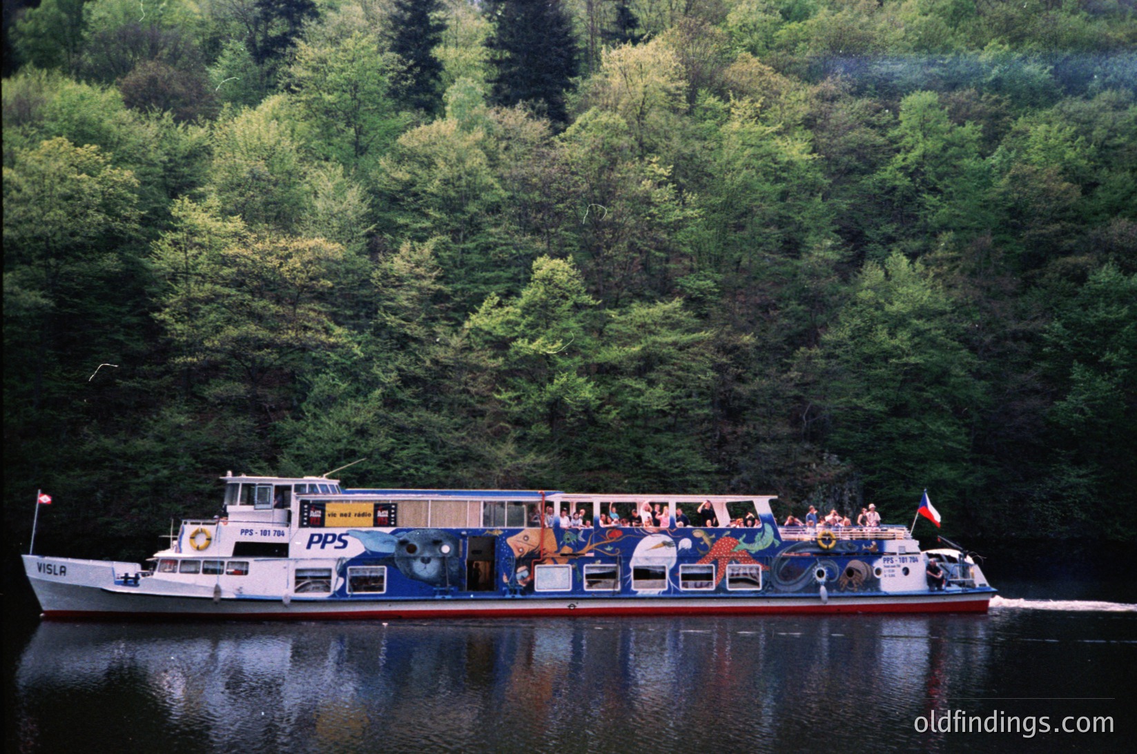 Passenger ferry "PPS" navigating a forested river, likely in Norway’s fjords. Mid-20th century design with open-air seating and lifebuoys. Lush greenery and calm waters reflect vessel’s hull. Ideal for travel, tourism, or historical maritime studies.