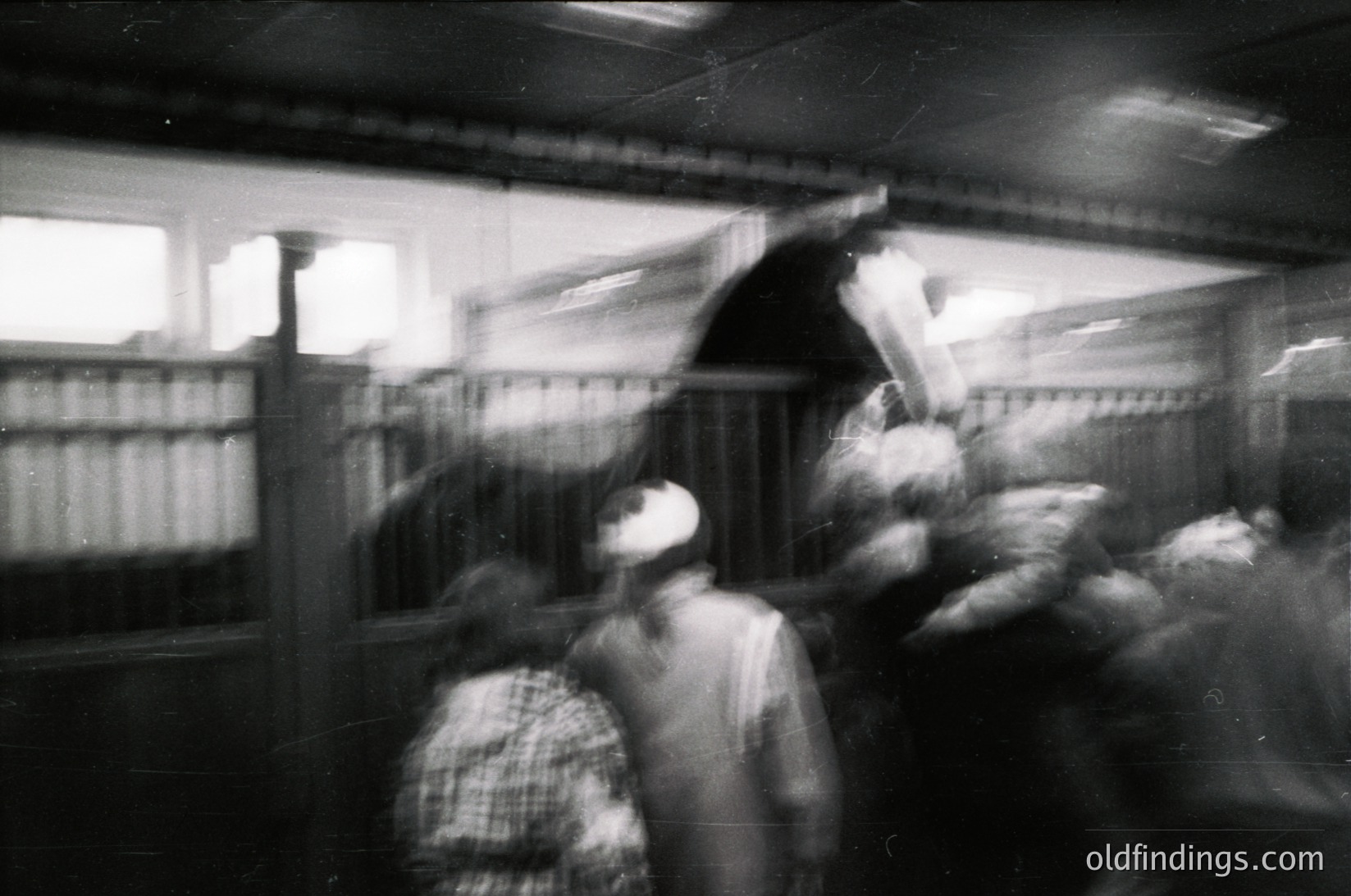 Blurred motion shot of a crowded indoor market, likely 1960s–1980s. Vendors in aprons and headscarves handle poultry, framed by wooden stalls. Warm lighting and close quarters suggest a bustling, communal atmosphere.