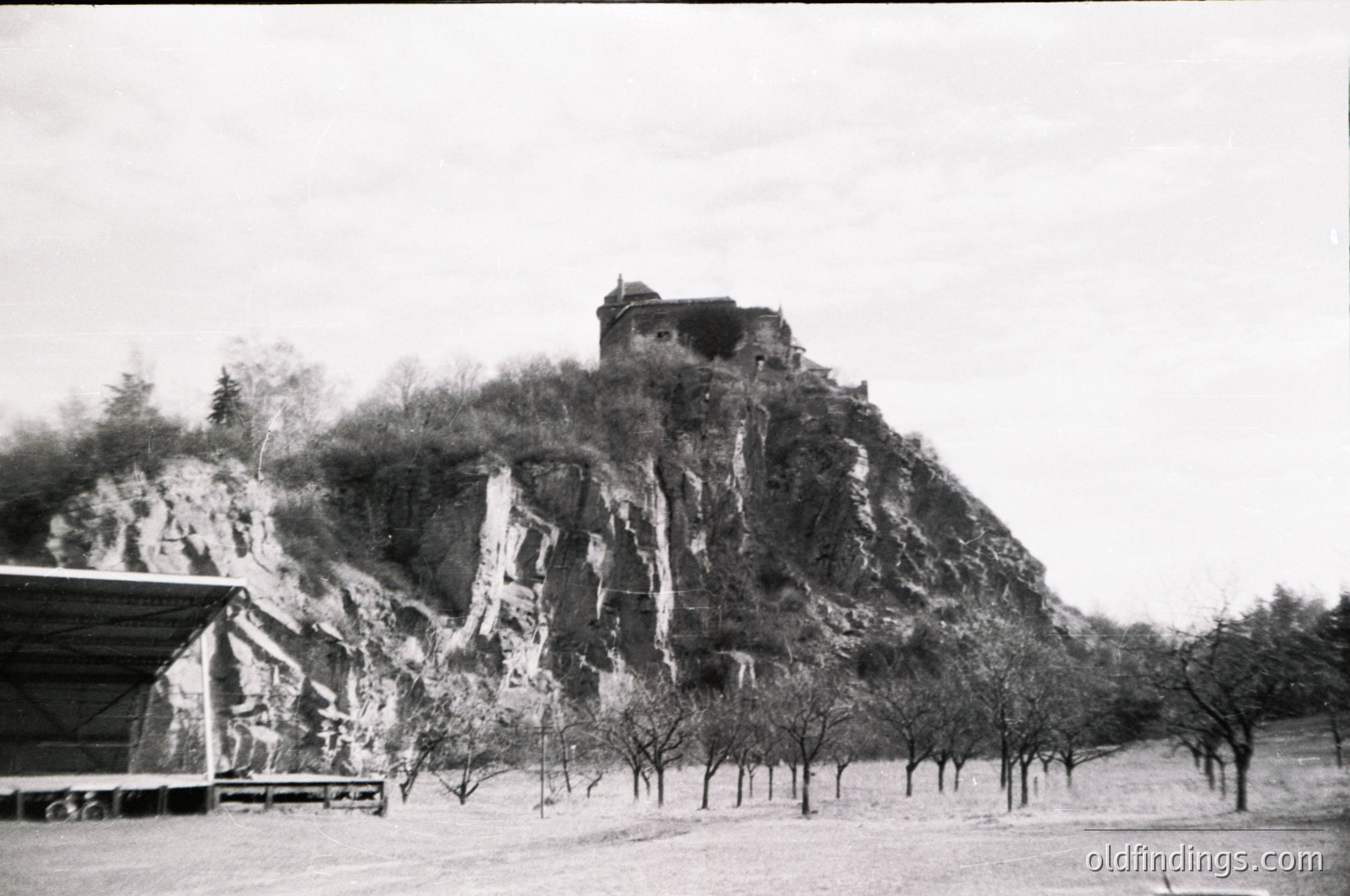 Historic stone fortress perched atop rugged cliff, surrounded by leafless trees in a mid-20th century black-and-white photo. Architectural ruins feature cylindrical towers and fortified walls.
