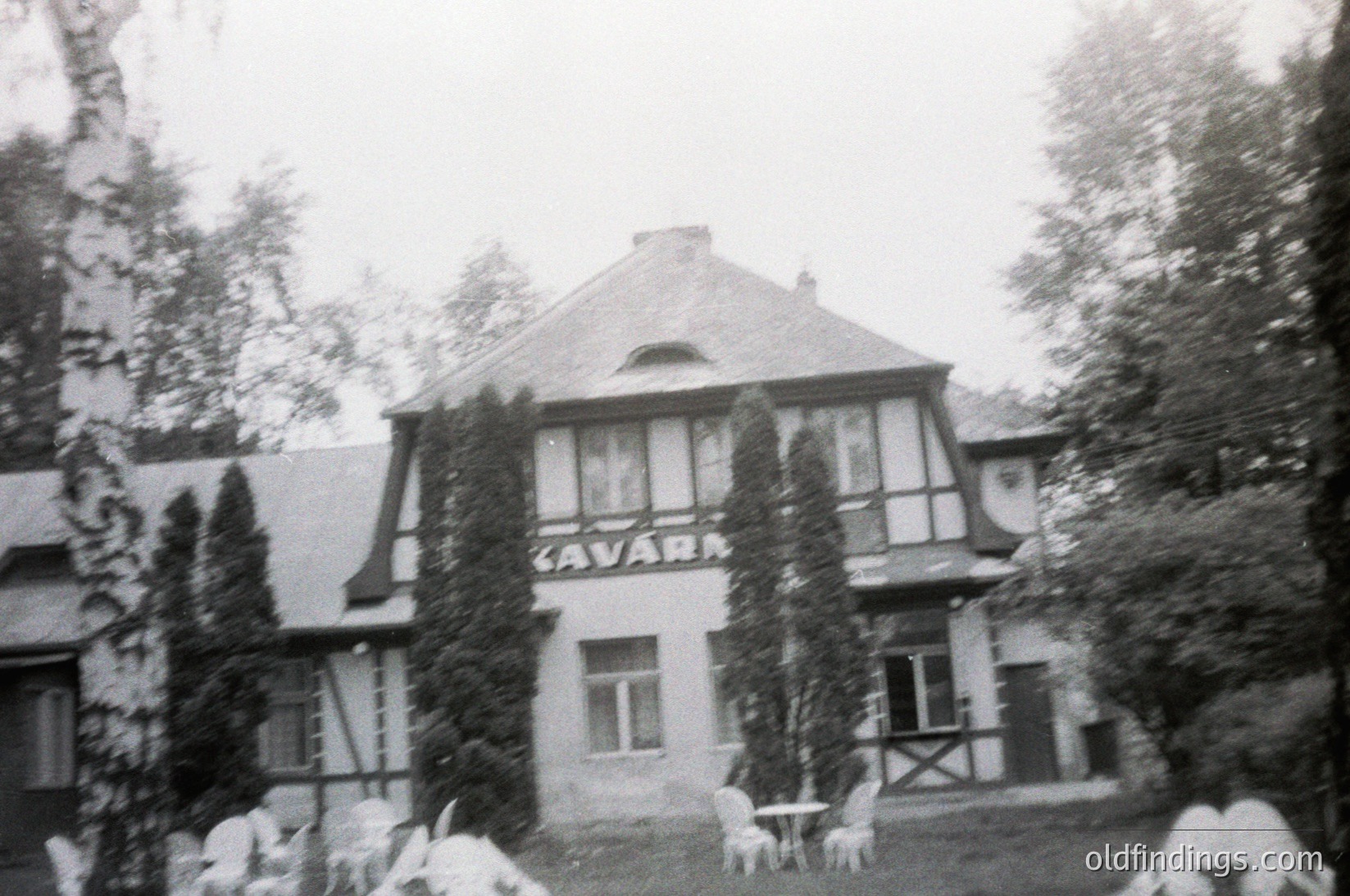 Vintage black-and-white photo of a two-story building labeled "CAVARA" in Art Nouveau-style lettering, featuring gabled roofs, large windows, and ivy-covered walls. Snow blankets the ground and rooftops, indicating a winter setting. Outdoor furniture and trees frame the scene, suggesting a resort or hotel.