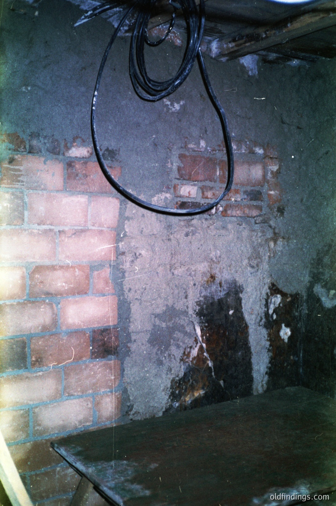 Vintage industrial interior featuring a rusted metal wall-mounted lamp with a cracked glass shade. Exposed brickwork with faded plaster reveals signs of wear, suggesting aged infrastructure. Likely a basement or utility space, with a concrete shelf below.